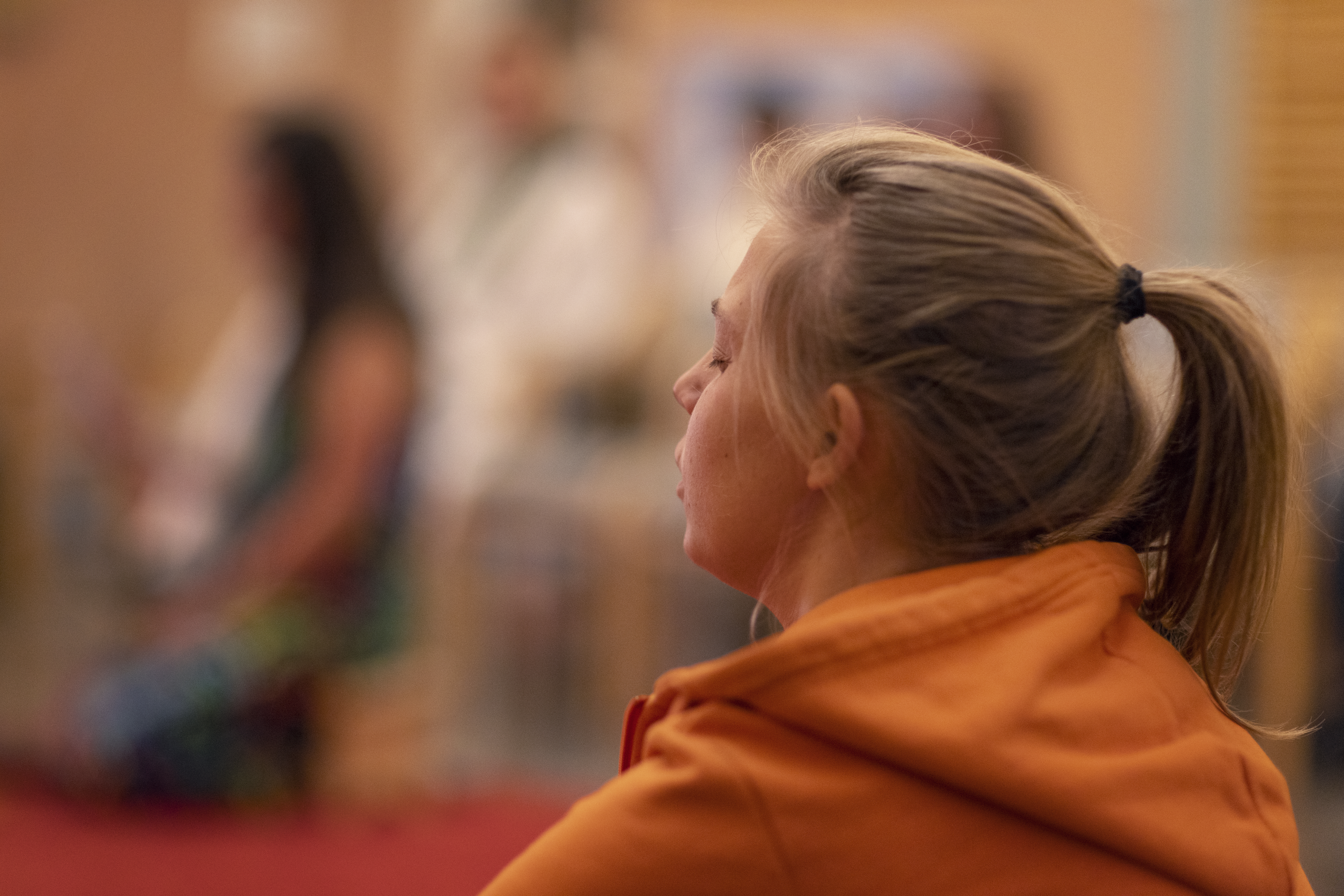 En kvinna i orange tröja och hästsvans sitter och blundar.