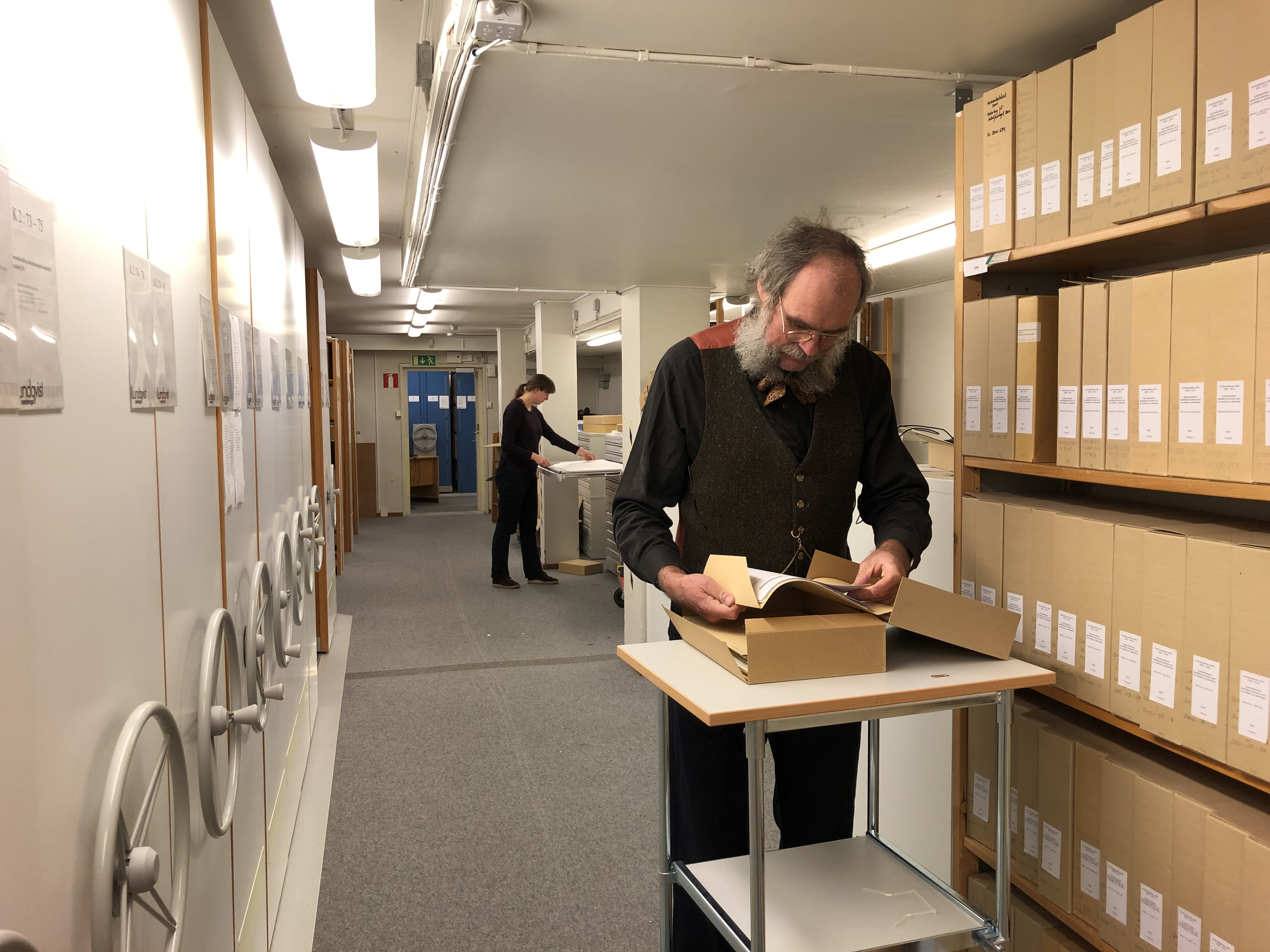 En kvinna och en man arbetar i ett arkiv.