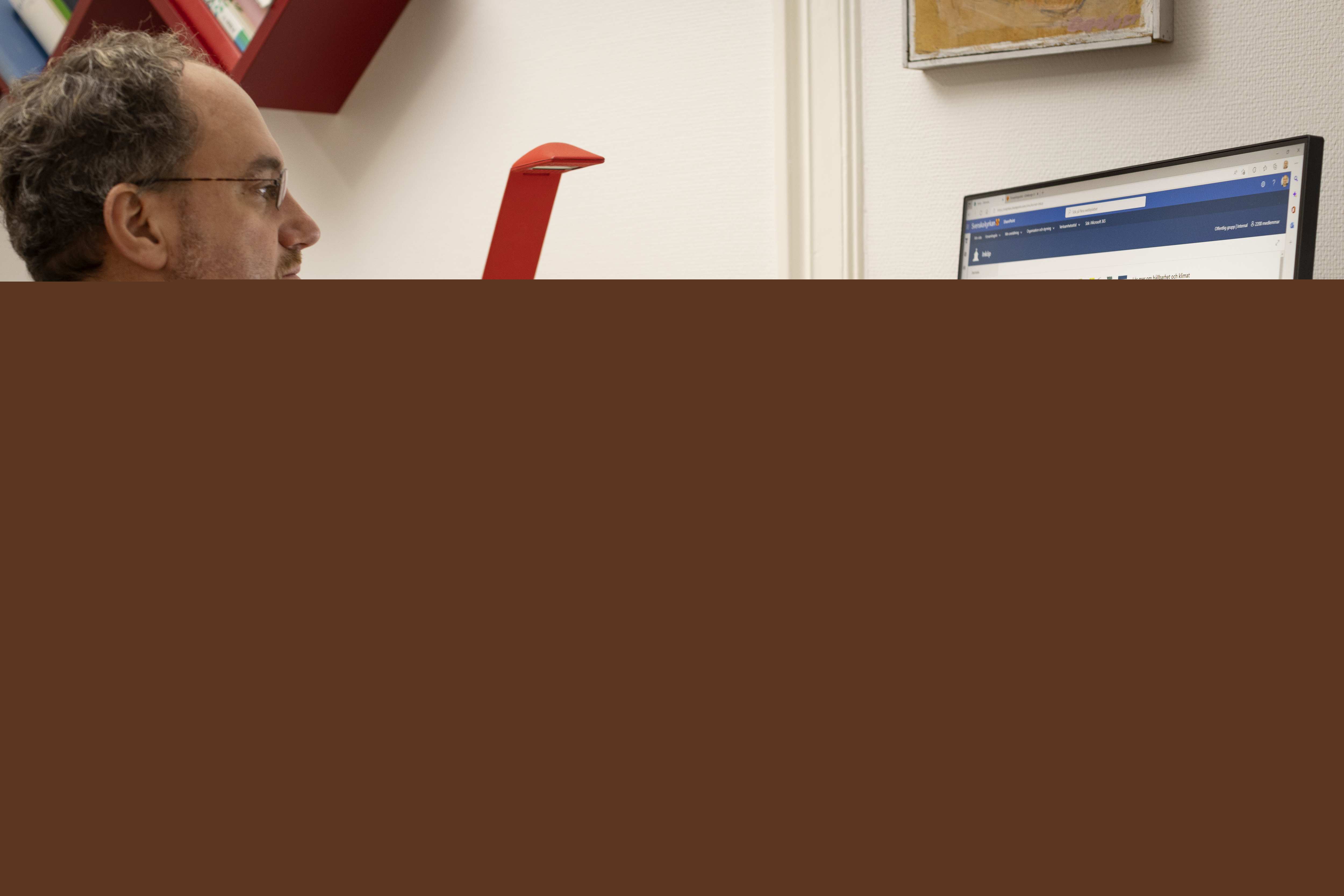 En man sitter vid ett skrivbord och arbetar i datorn.