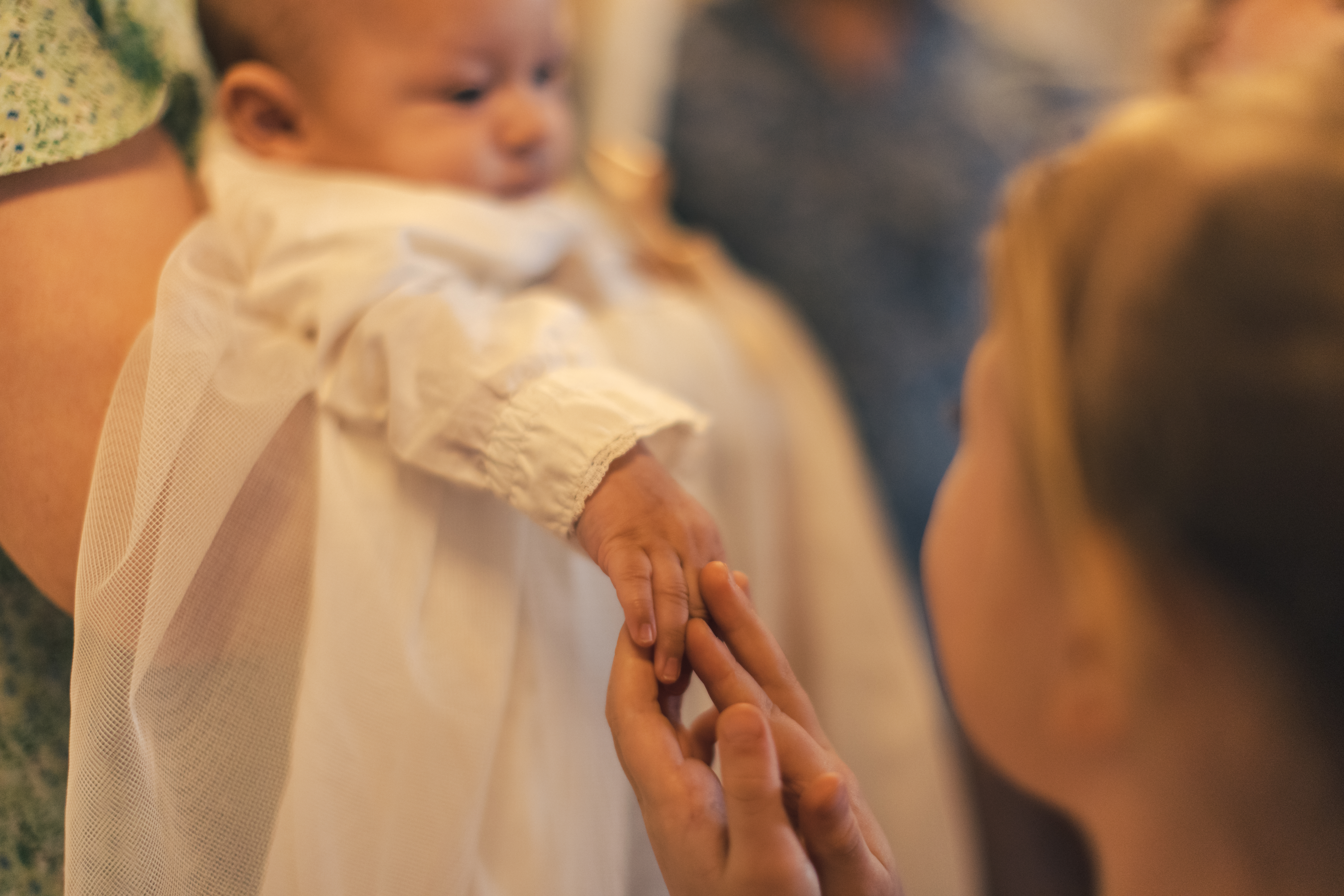 En bebis i dopklänning. Någon håller i barnets hand.