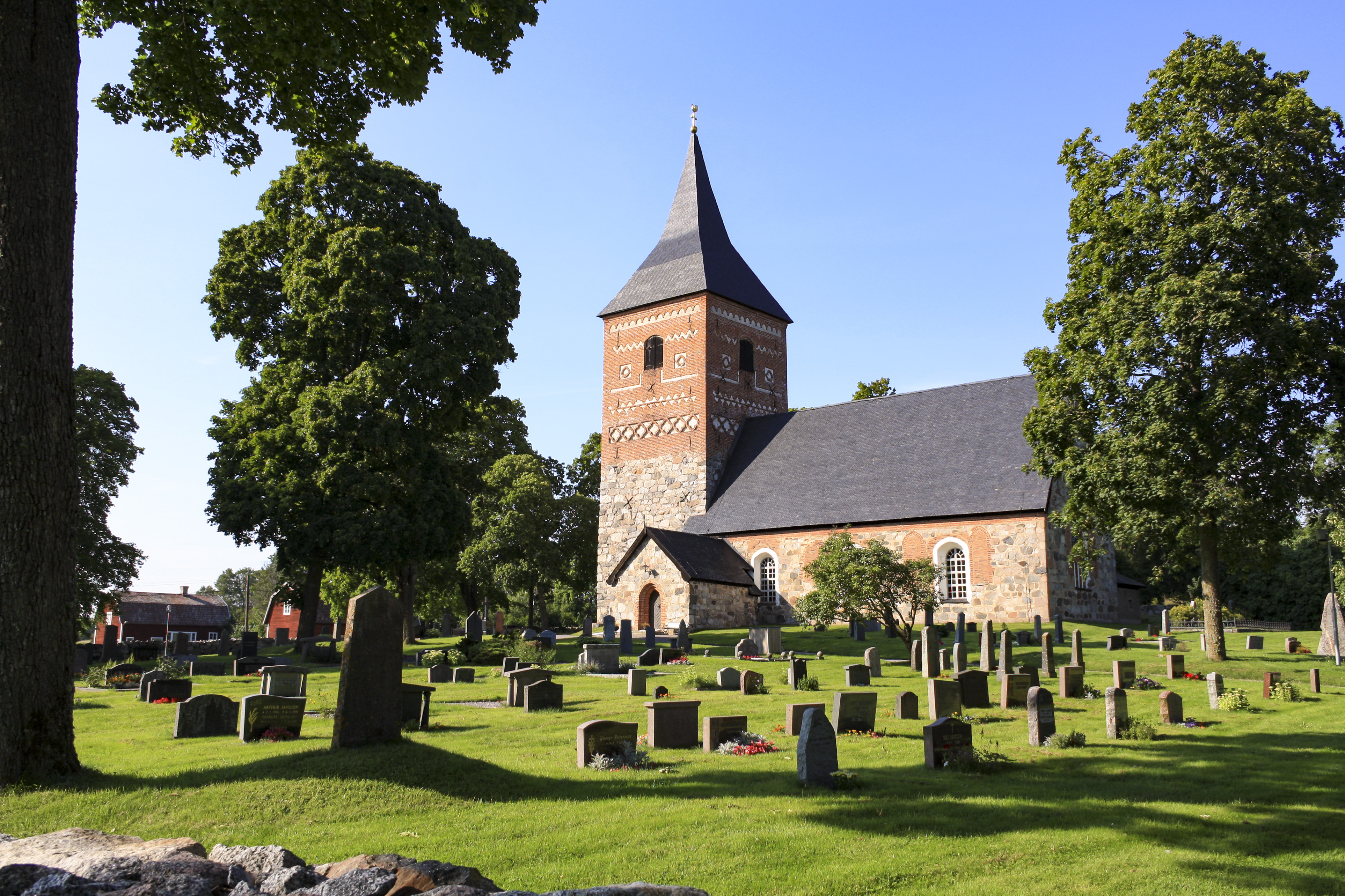 En kyrka i sten och rött tegel. Gravstenar på en grön gräsmatta.