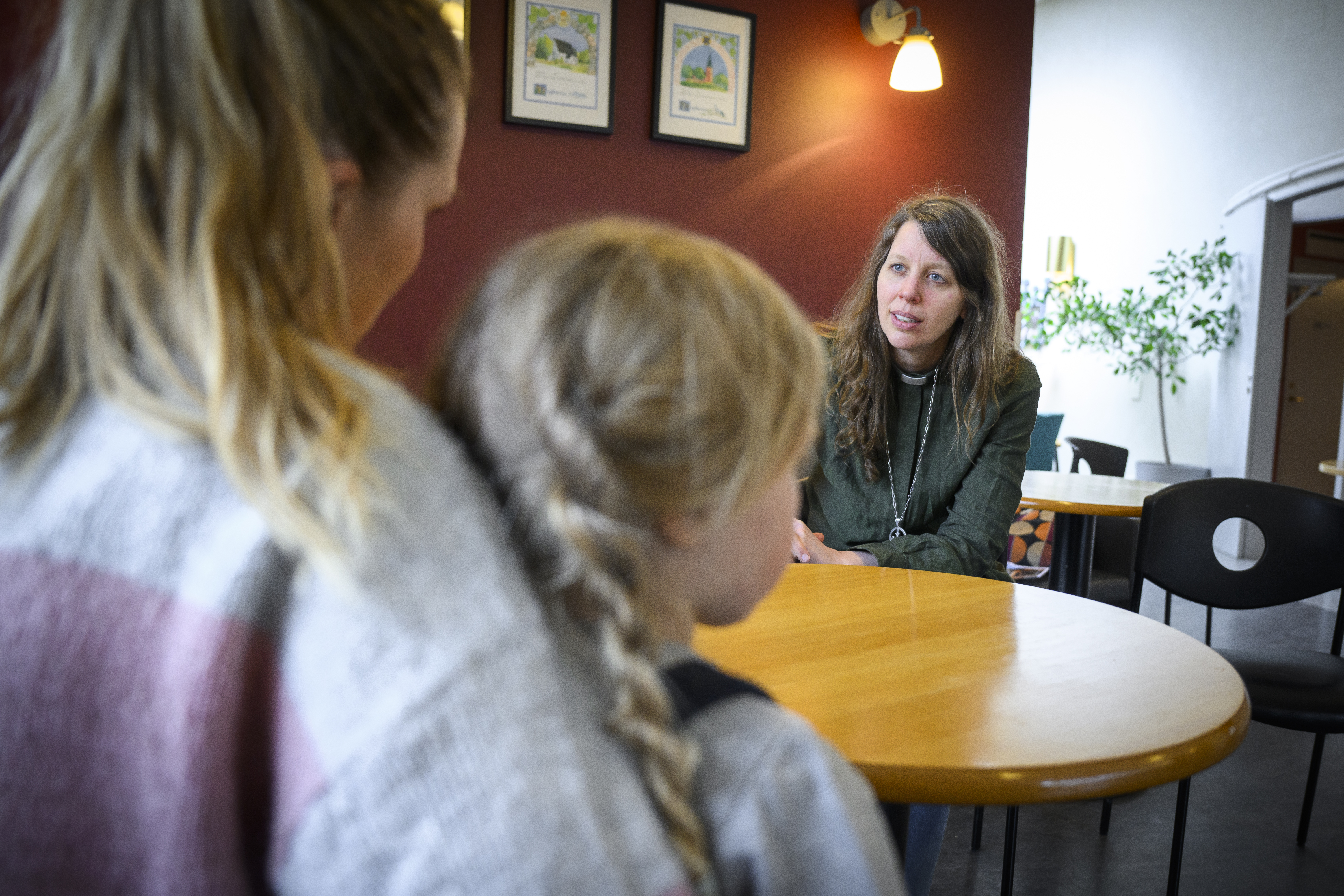 En diakon sitter och samtalar med en kvinna med en liten flicka i knät.