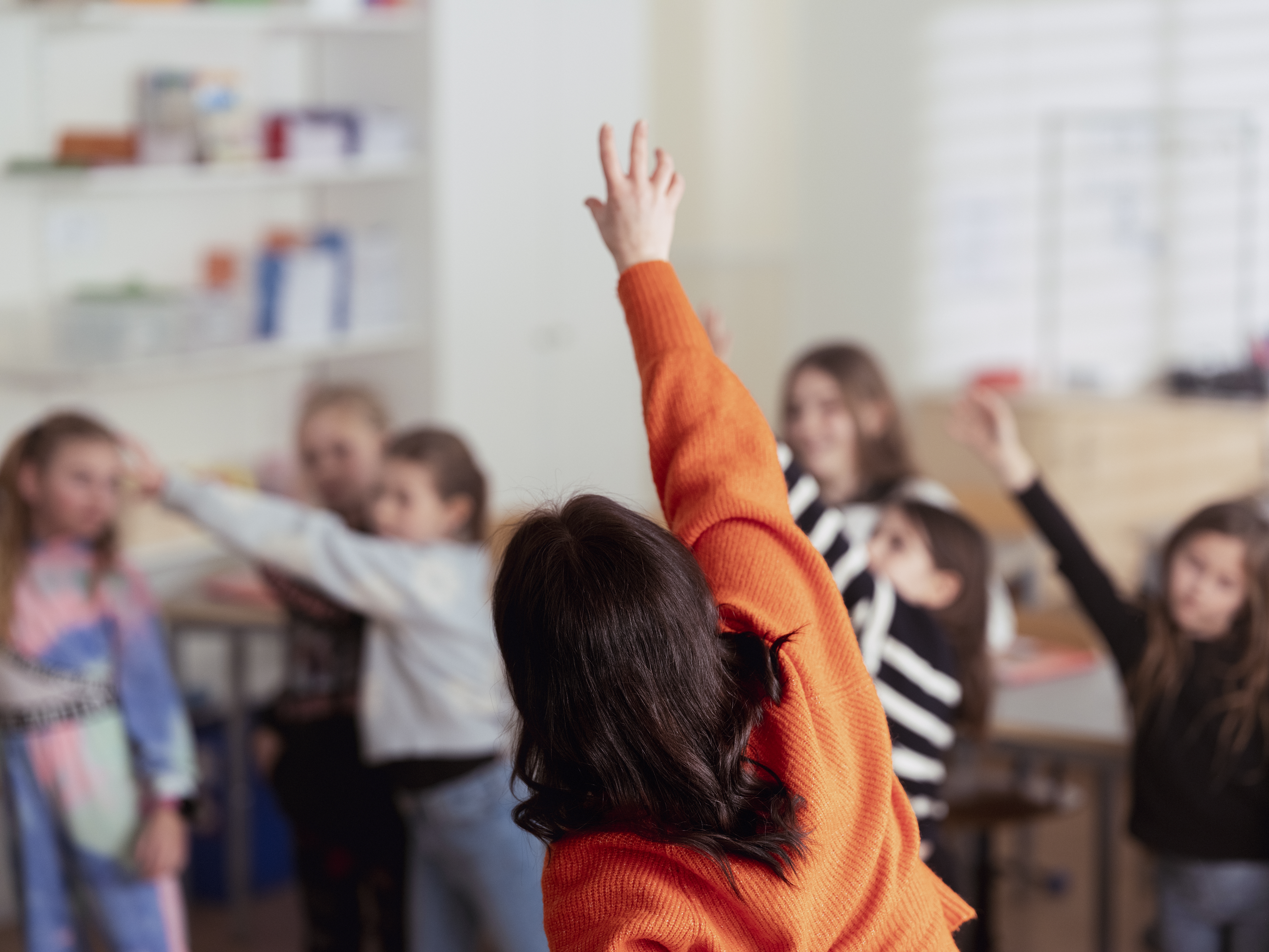 En kvinnlig körledare står framför en barnkör och sträcker upp en arm i luften.