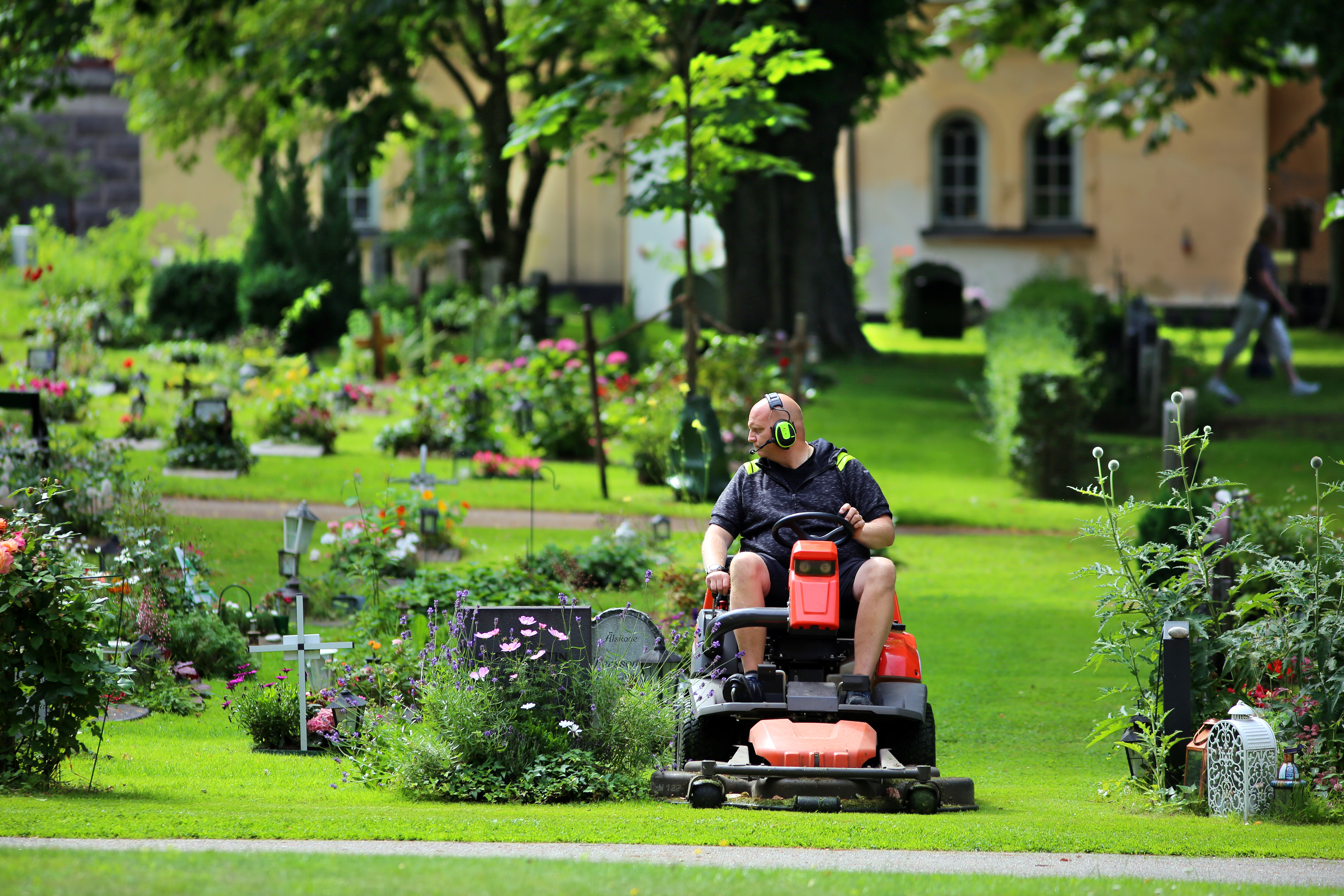 En kyrkogårdsarbetare klipper gräset runt gravstenarna med en åkgräsklippare.