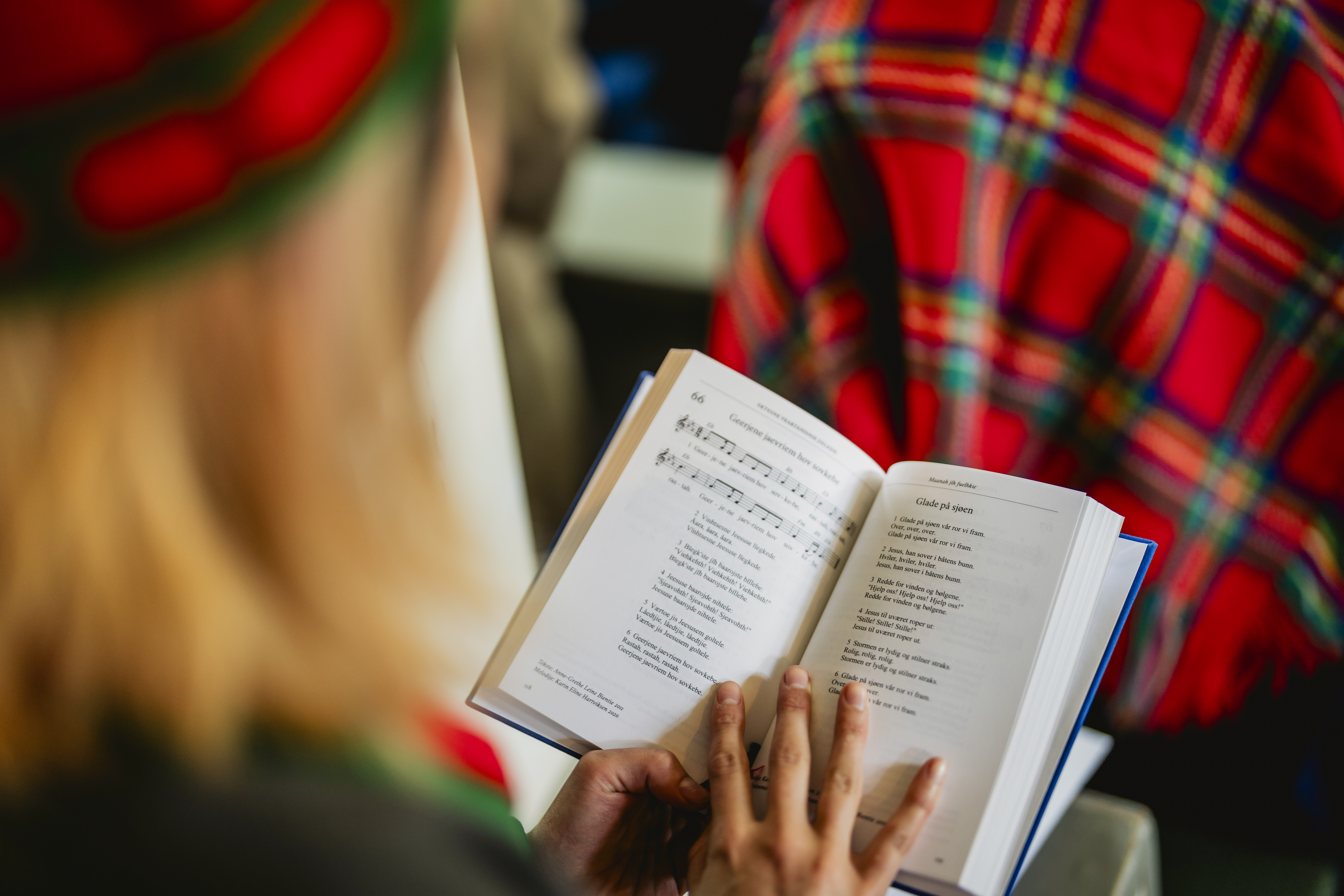 En kvinna i en kyrkbänk har en uppslagen psalmbok i knät.