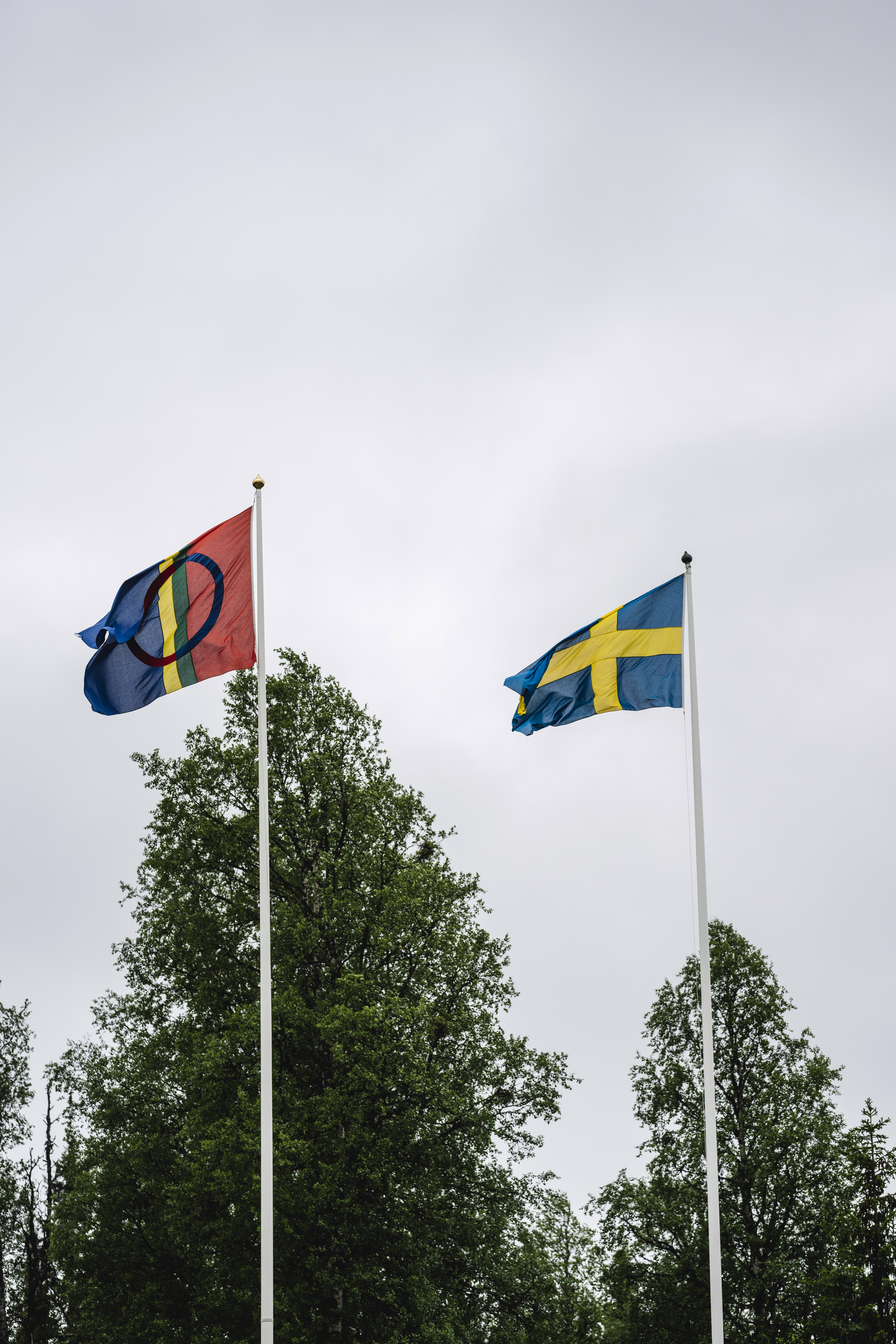 Två flaggstänger med den samiska flaggan och Svenska kyrkans flagga mot en grå himmel.