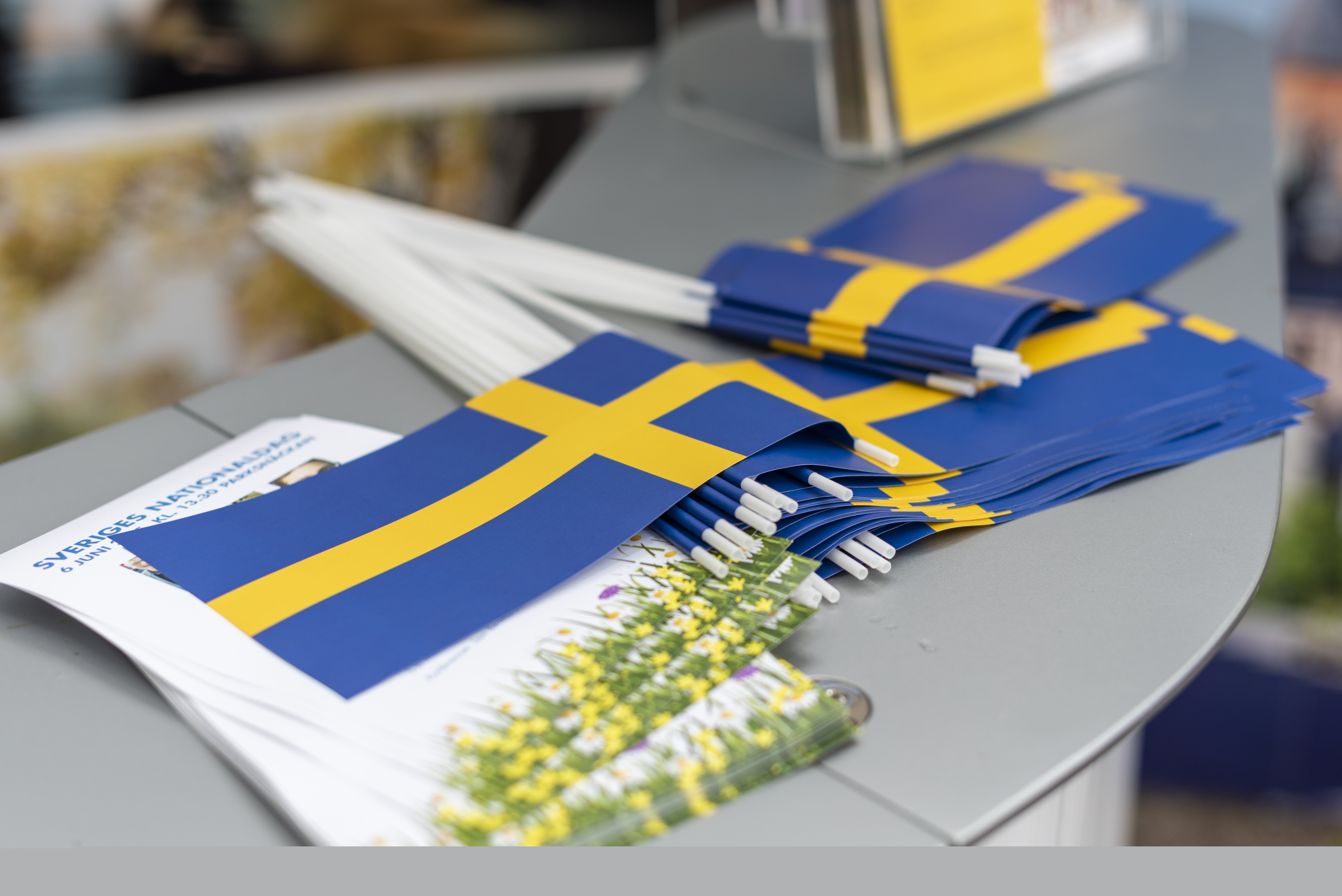 En hög med svenska flaggor och tryckta blad med texten Sveriges nationaldag ligger på en bänkyta.