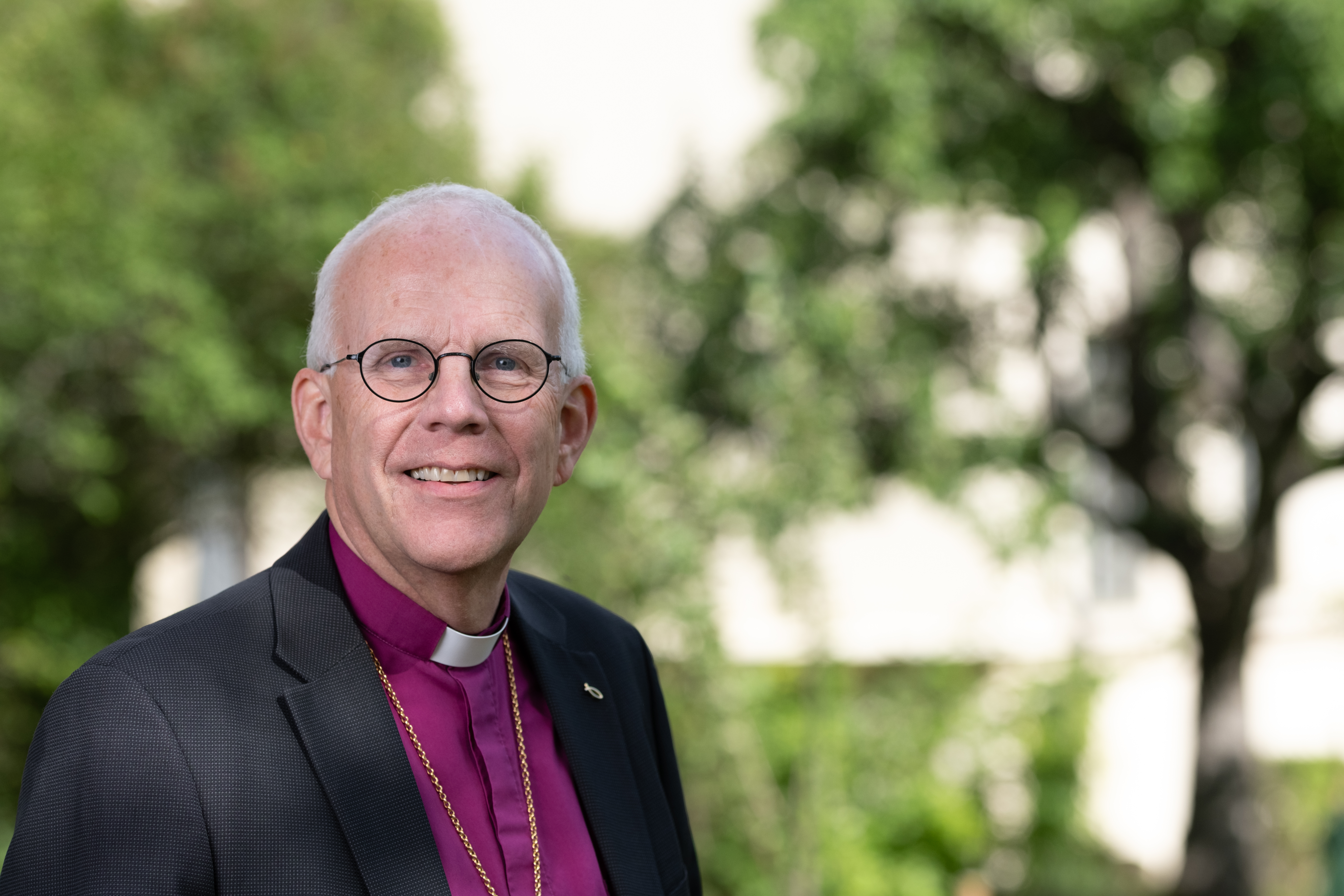 Porträttbild utomhus på ärkebiskop Martin Modéus i lila biskopsskjorta och svart kavaj.