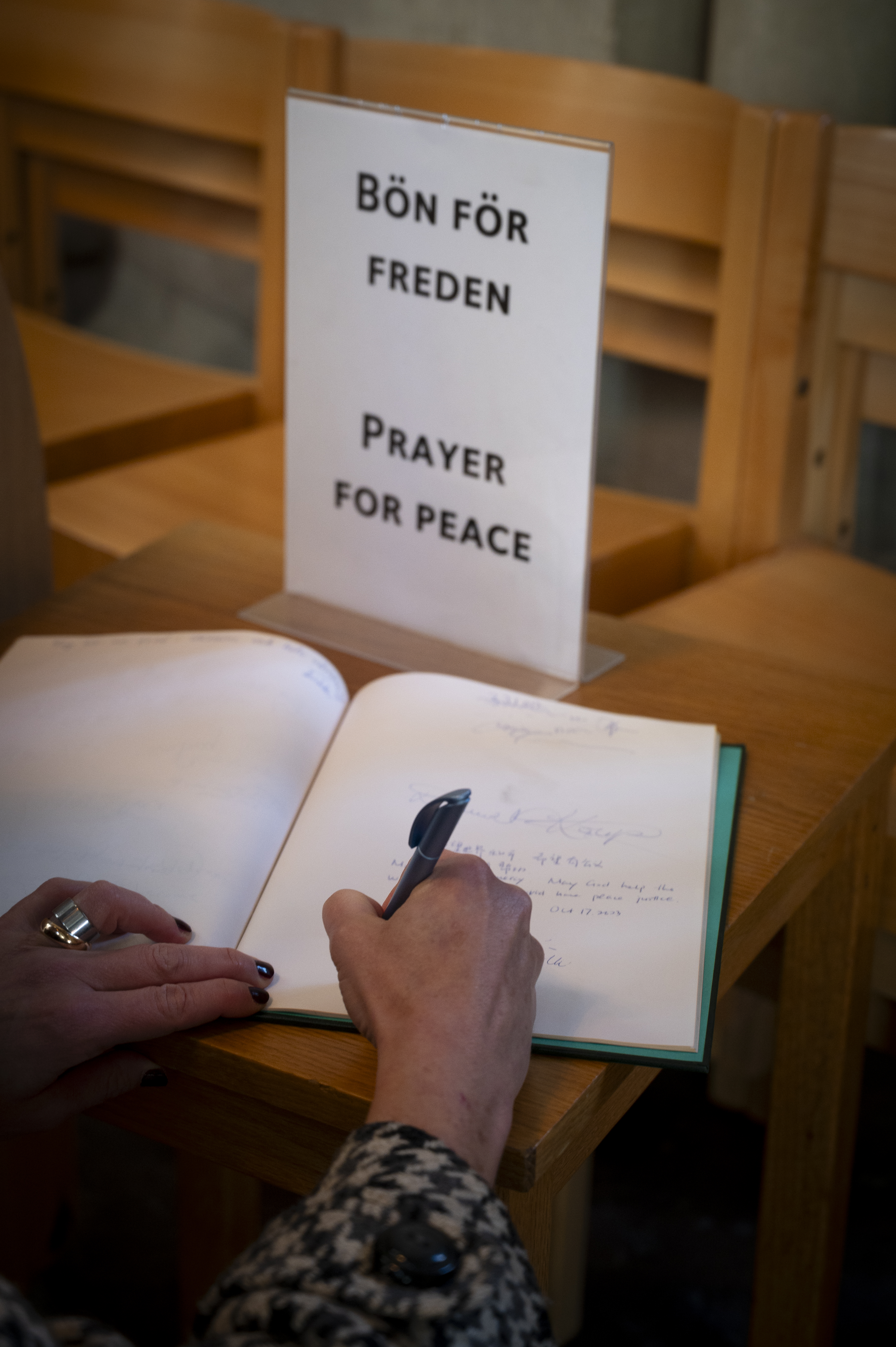 Någon skriver i en bok med blanka blad. En skylt med texten Bön för freden står bredvid.