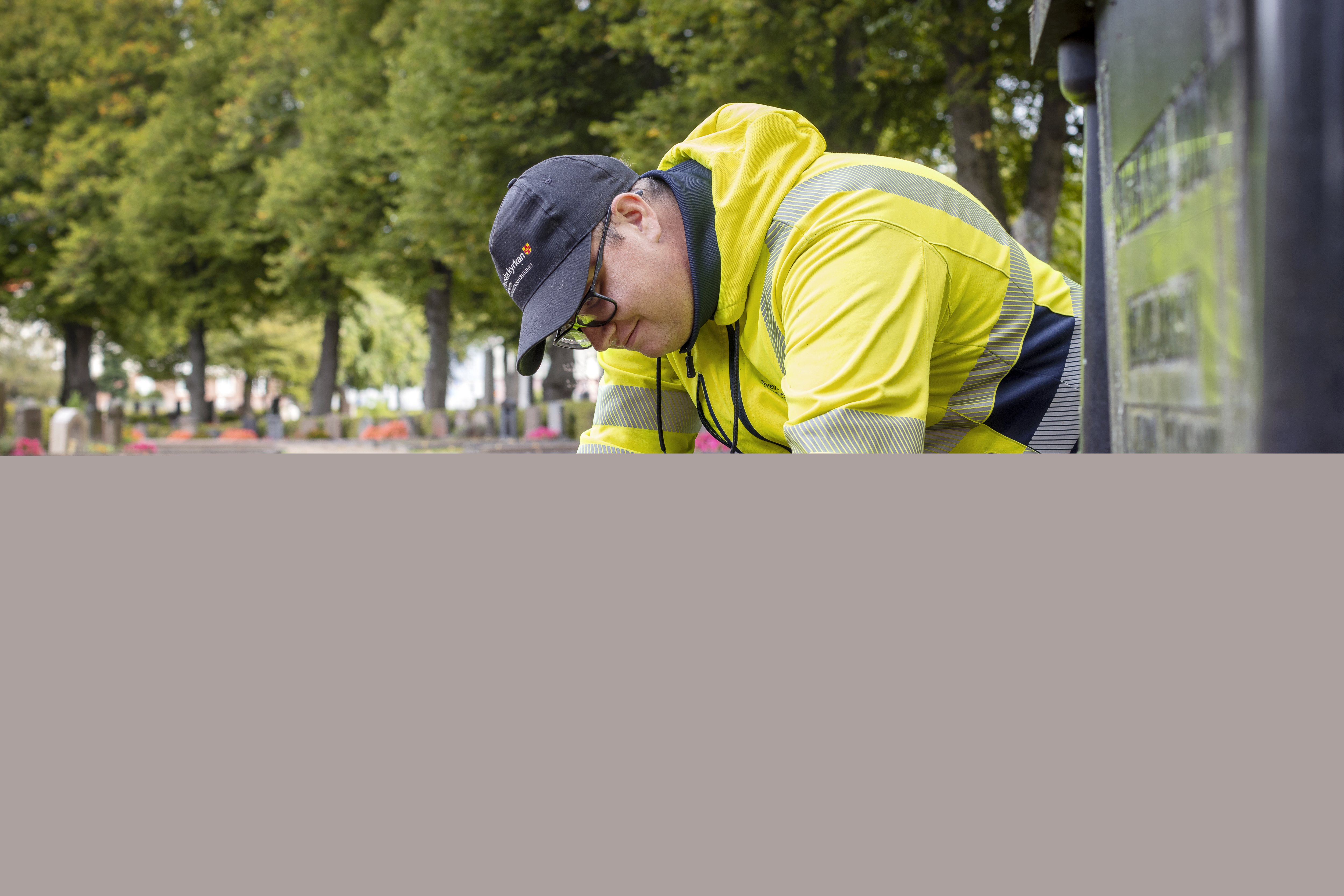 En kyrkogårdsarbetare i gula varselkläder fixar blommorna på en gravplats.