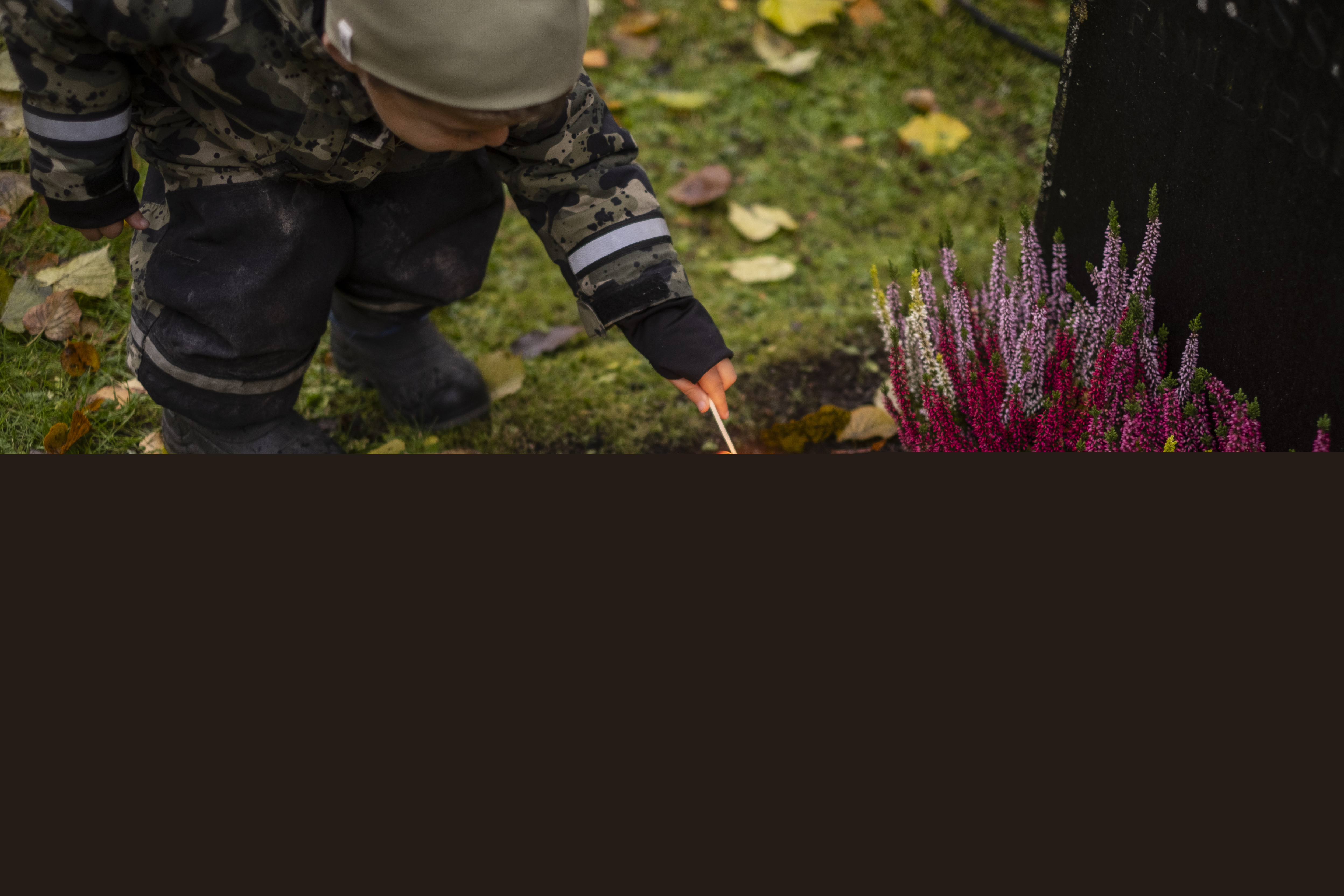 Ett litet barn tänder ett ljus vid en gravsten.