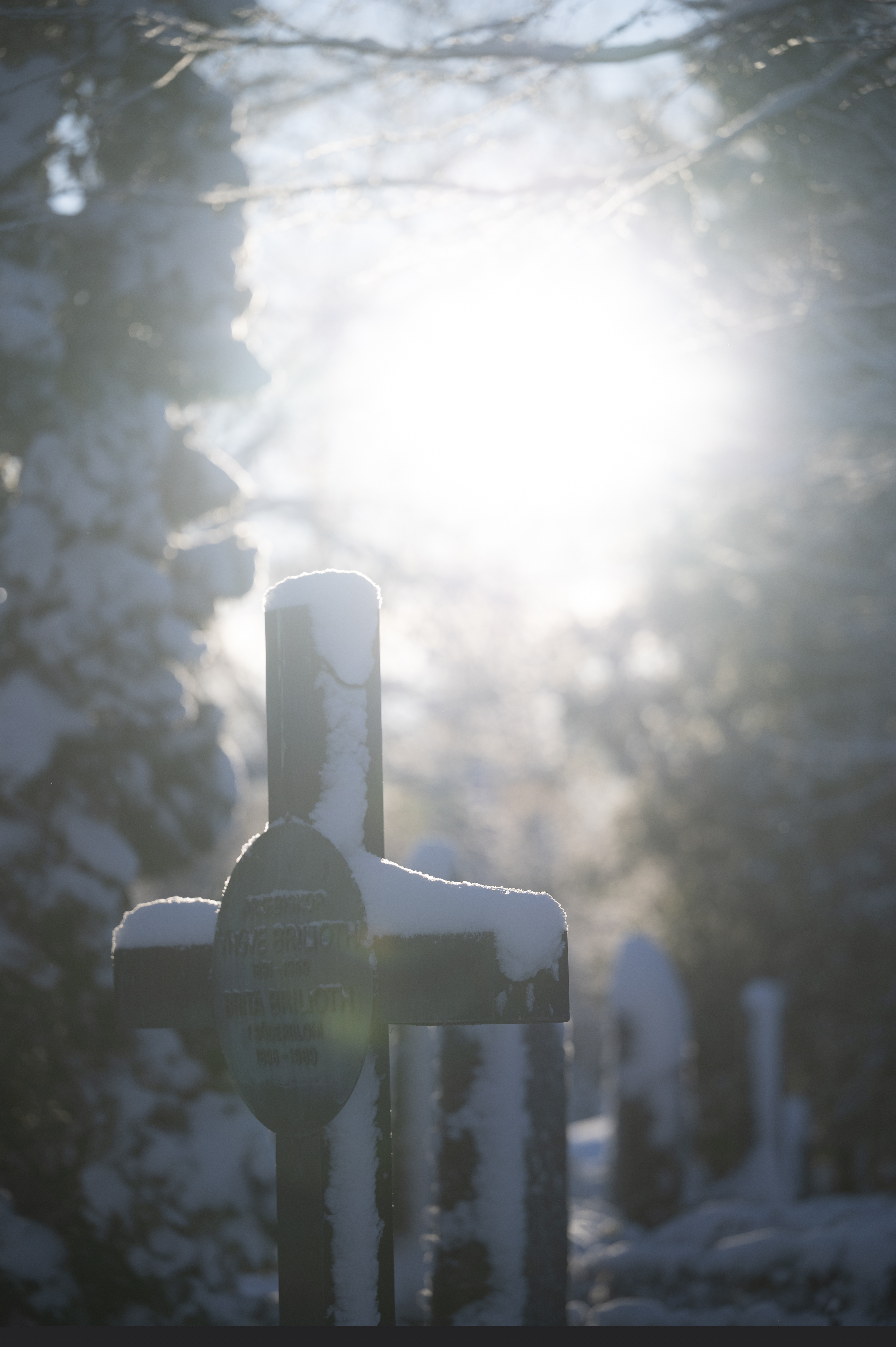 Snö ligger på en gravsten. Solen lyser.