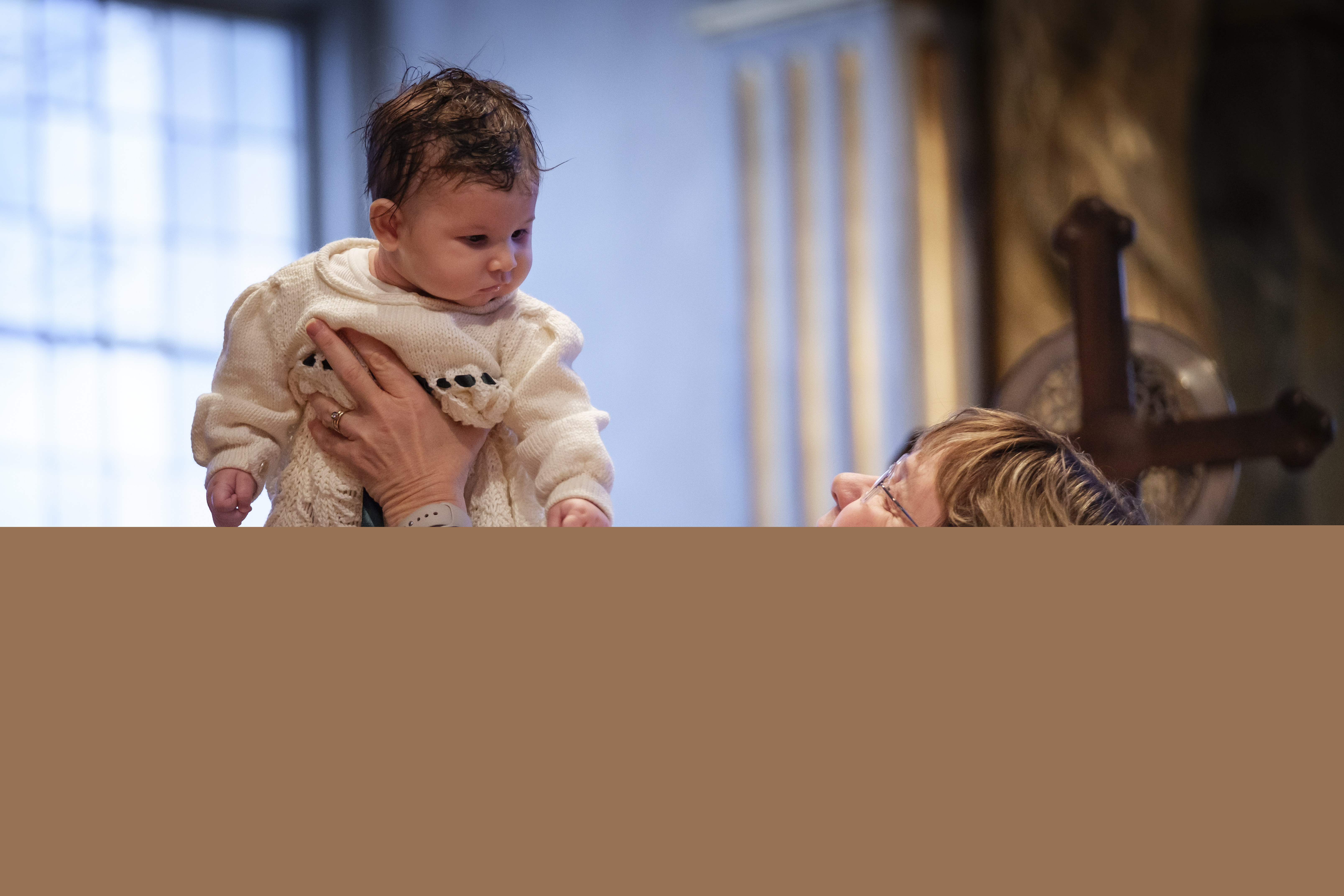 En kvinnlig präst håller upp en bebis som precis har döpts.