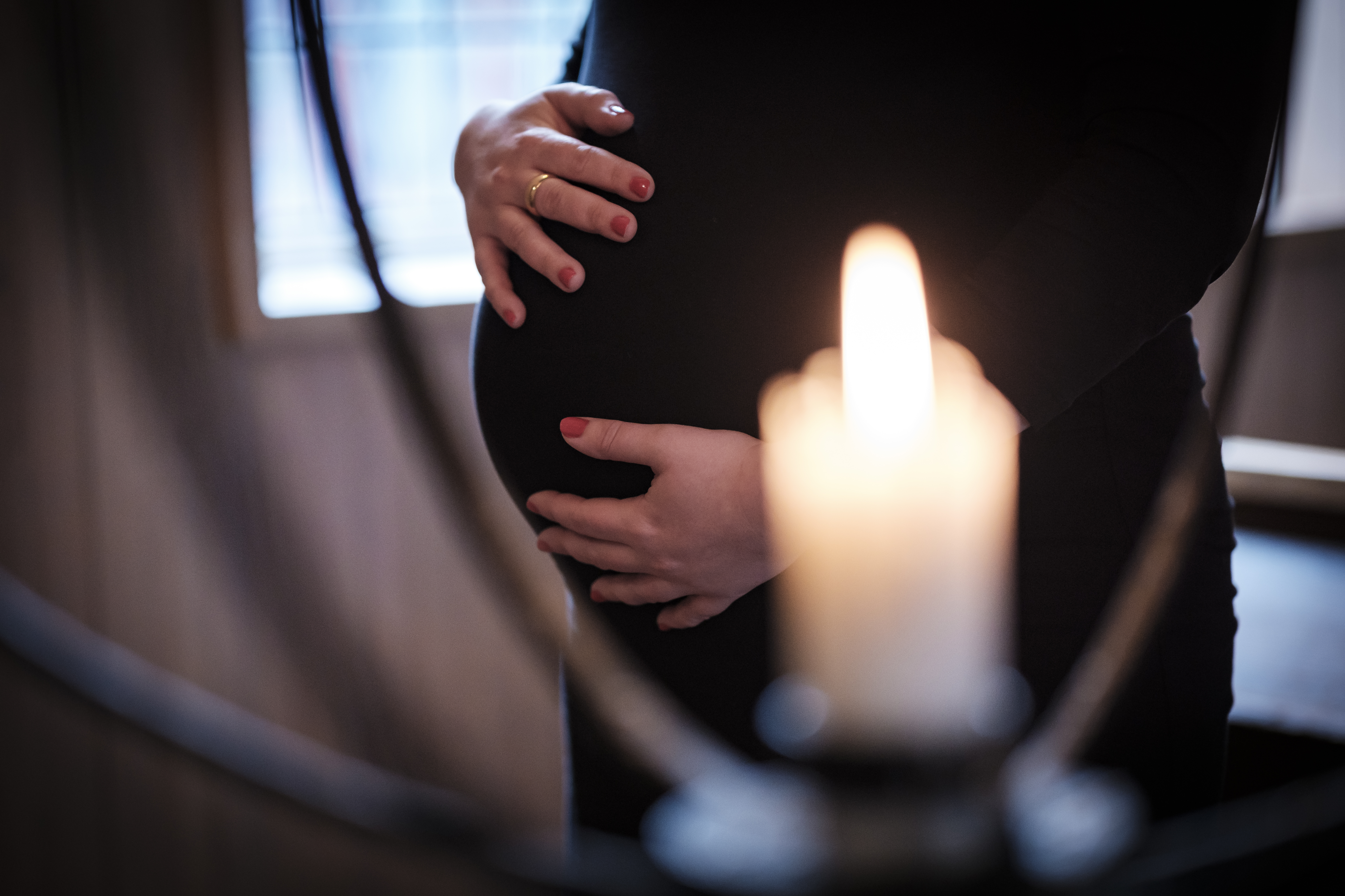 En gravid kvinna har sina händer på sin mage. Ett suddigt ljus i förgrunden.