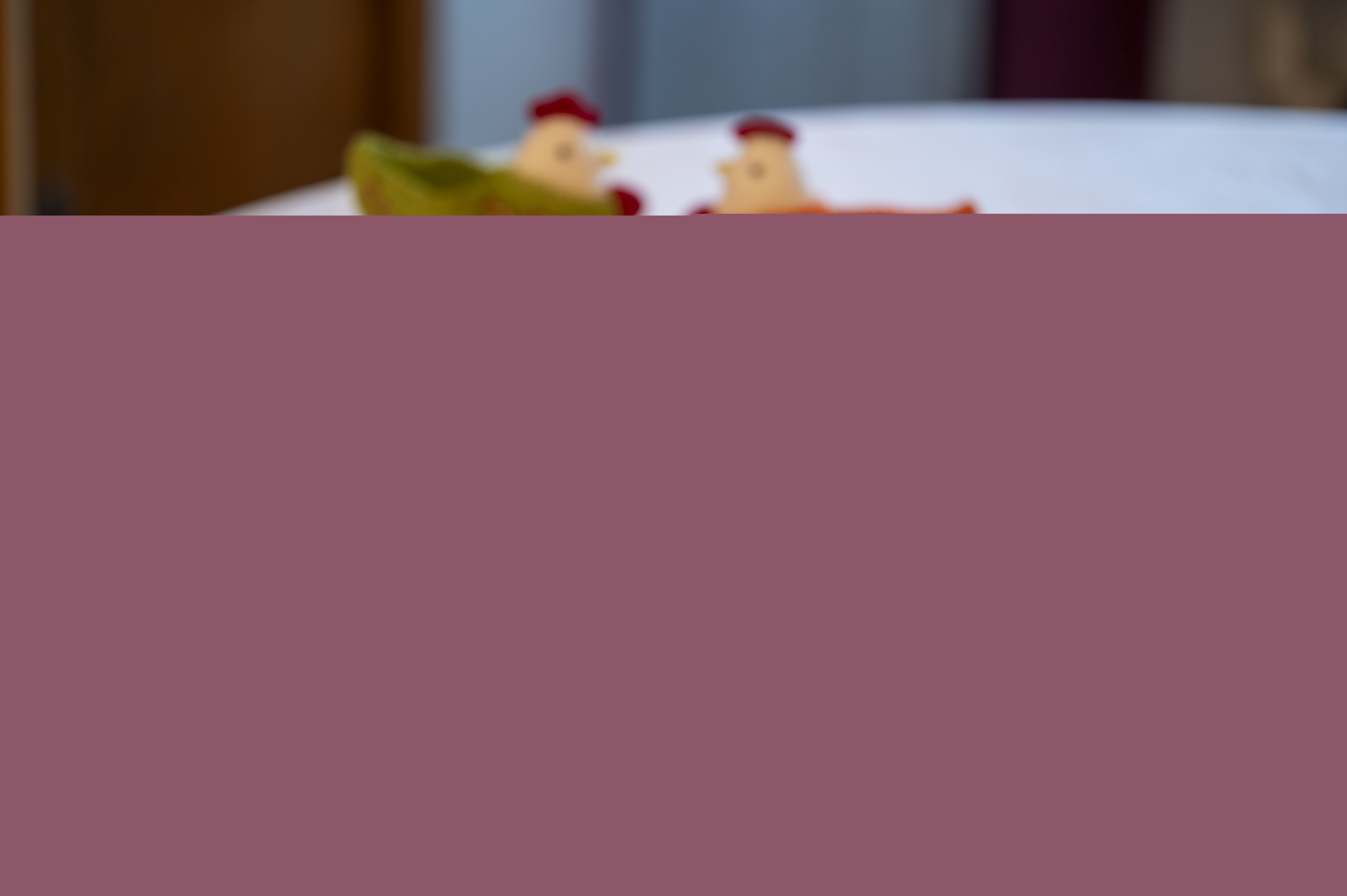 Ett kakfat, två kaffekoppar på fat och två påskhönor med ägg står uppdukade på en gul duk.