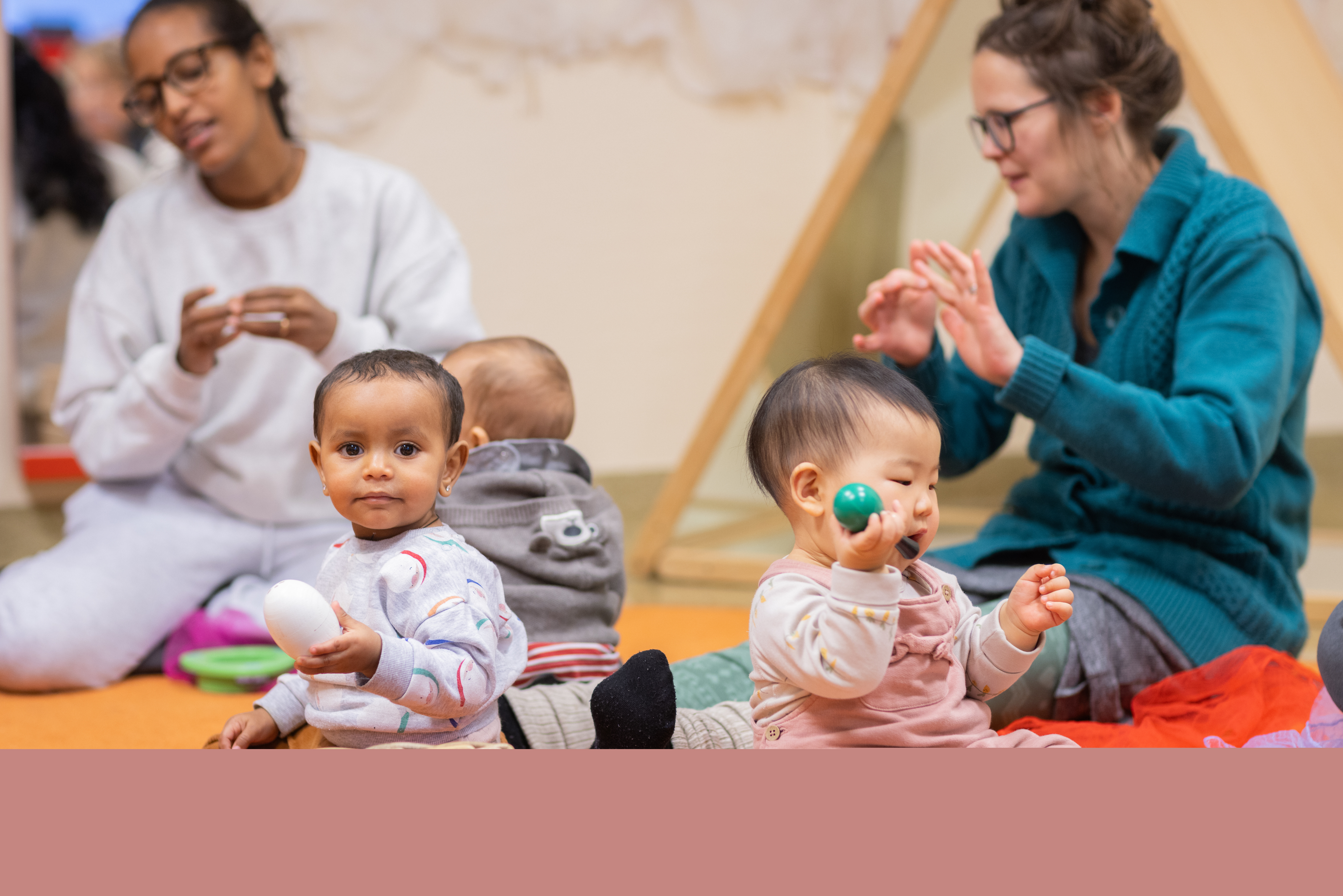 Tre bebisar sitter på golvet. Runt om sitter deras mammor och sjunger.