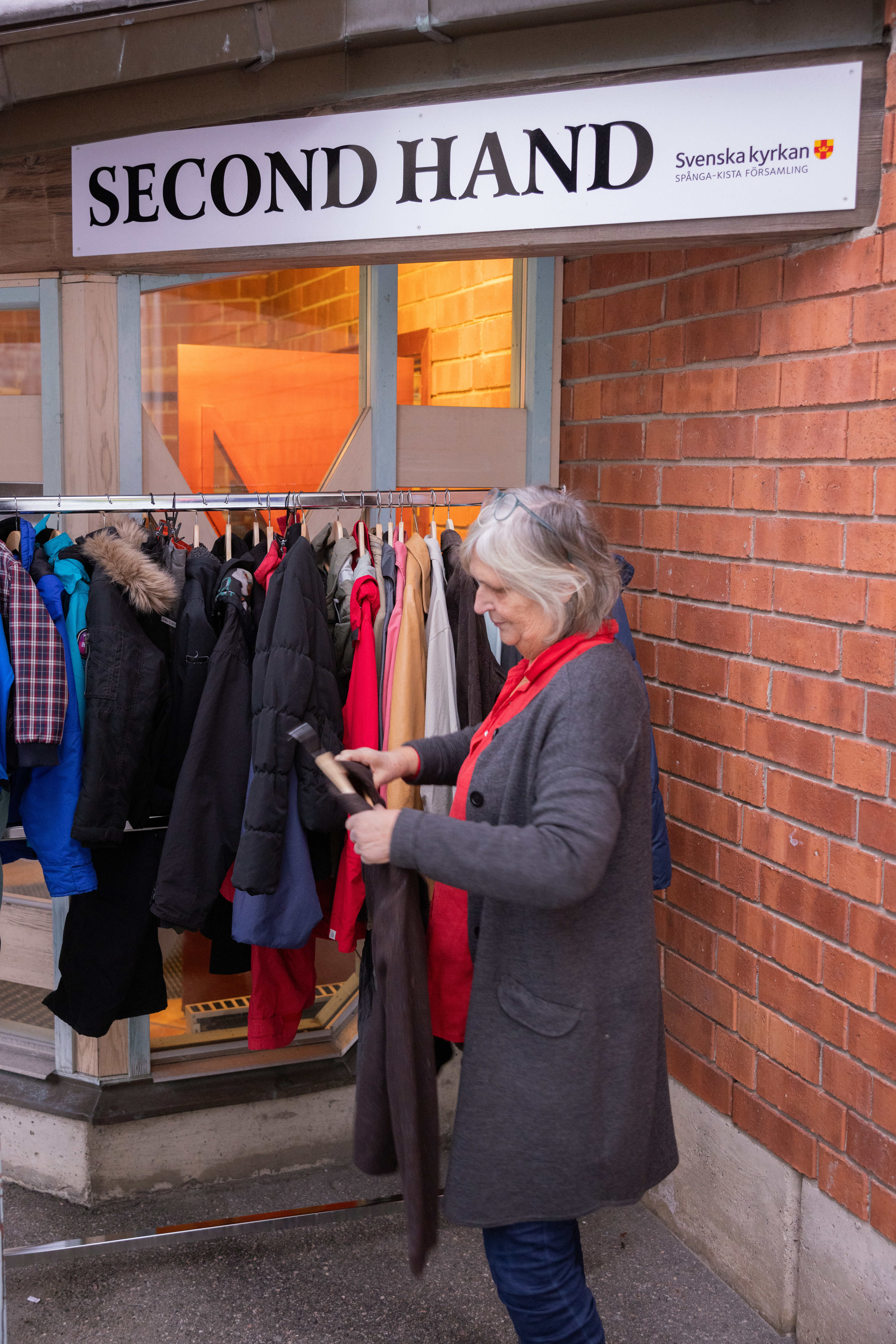 En kvinna hänger upp en tröja på en ställning utanför dörren till en second hand-butik.