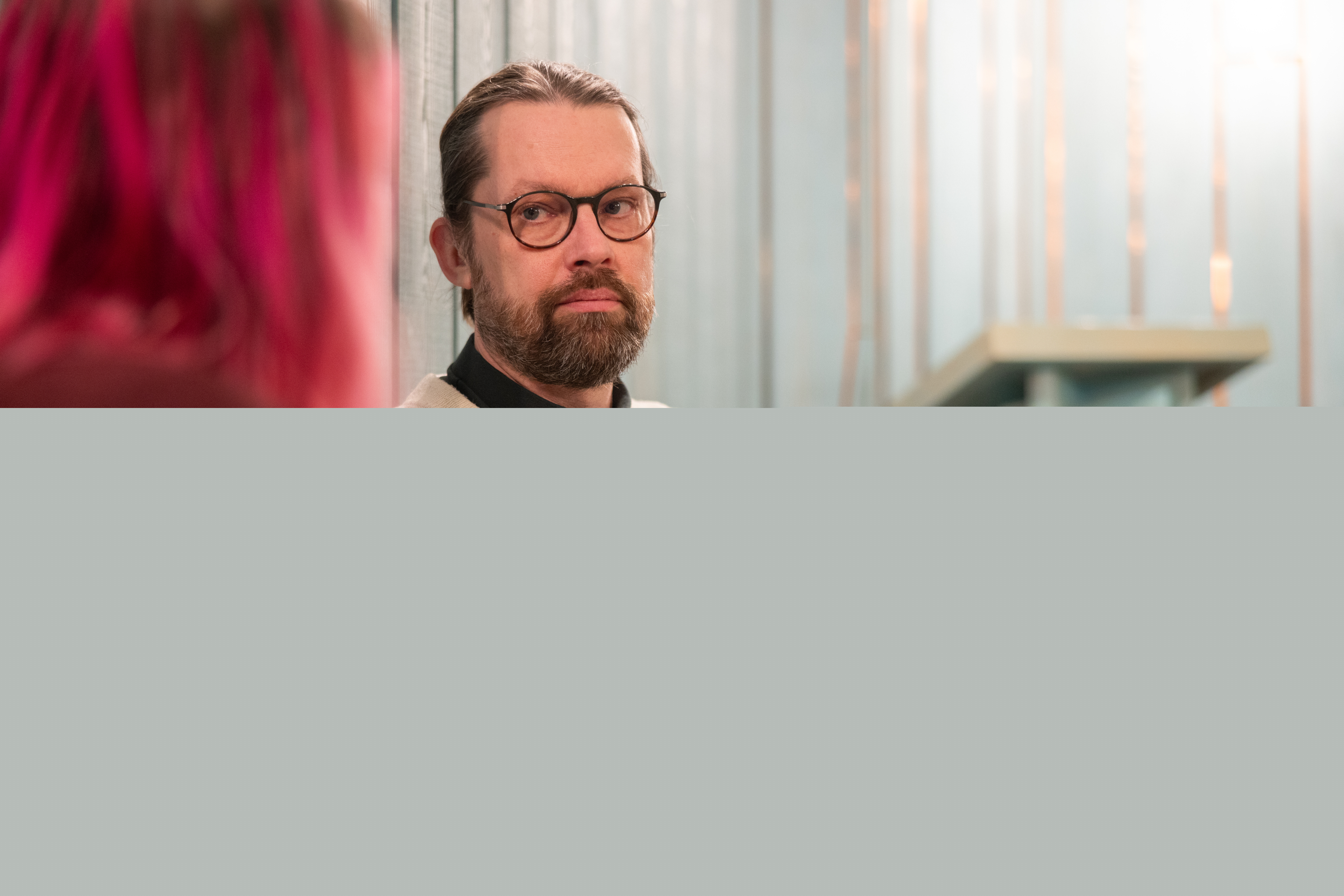 En diakon sitter inomhus och samtalar med en person med rosafärgat hår.