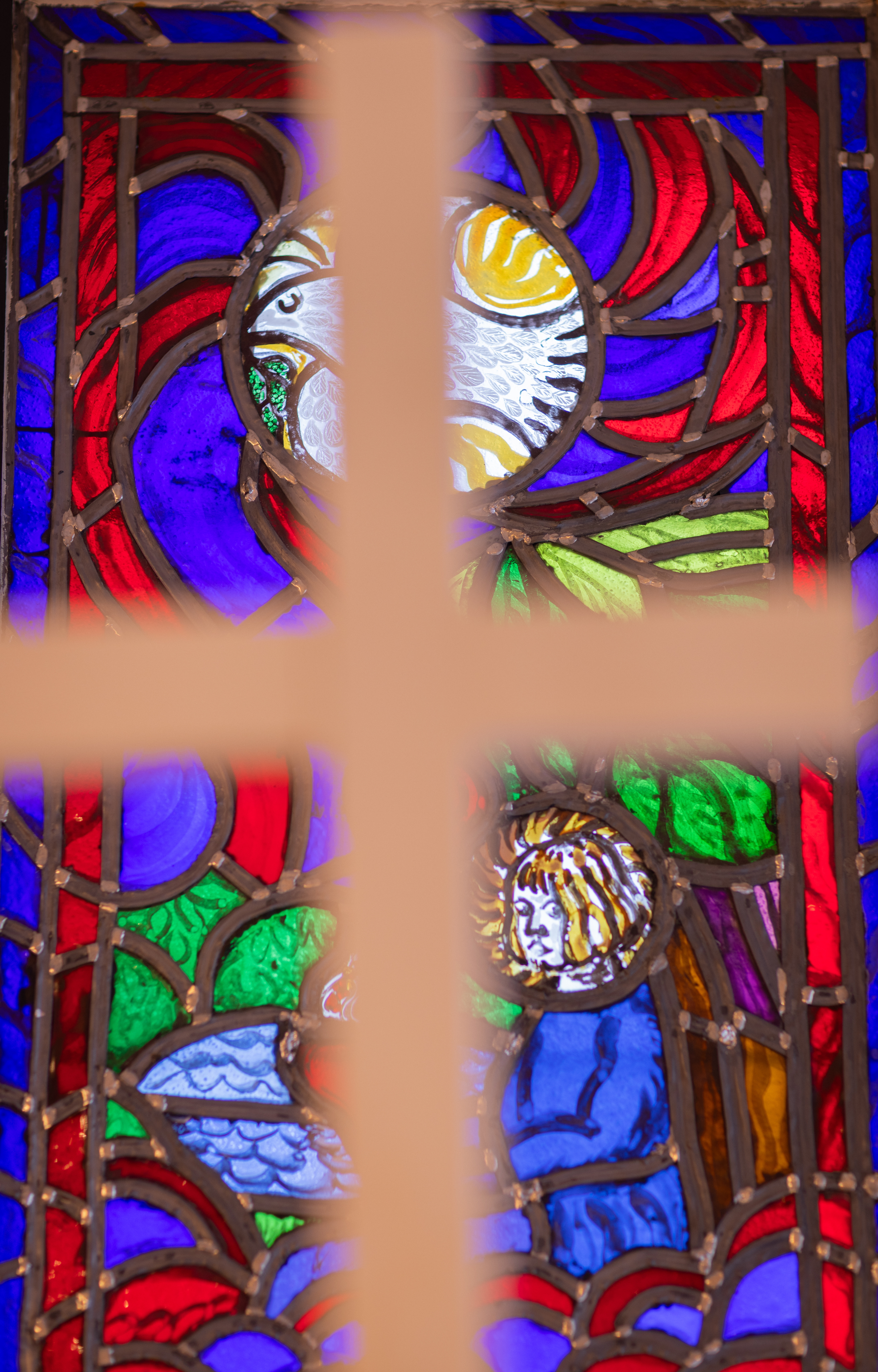 Ett oskarpt kors i förgrund av ett kyrkfönster, vi ser en fredsduva i glaset.