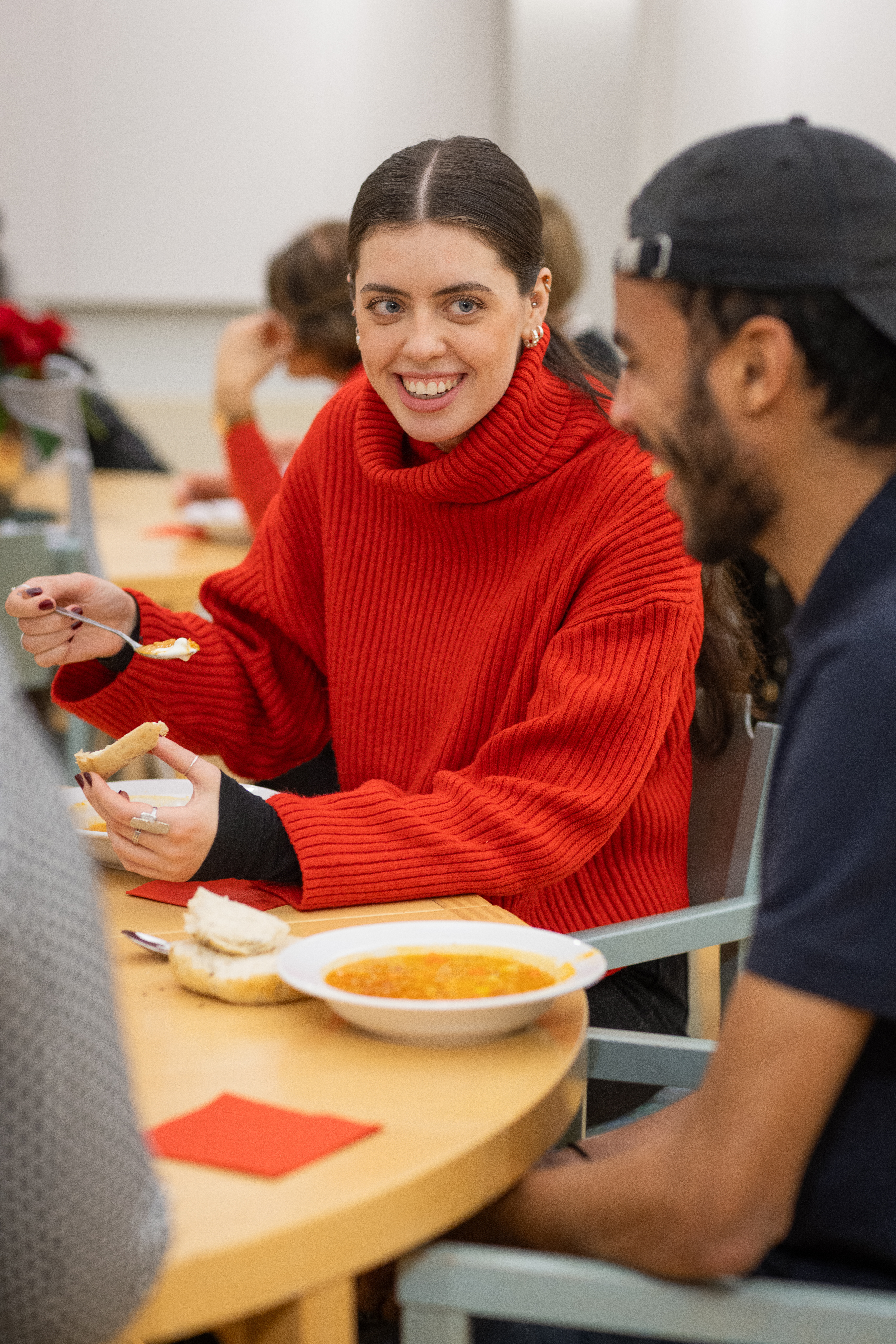 En kvinna vid ett matbord tar skrattande en sked soppa.