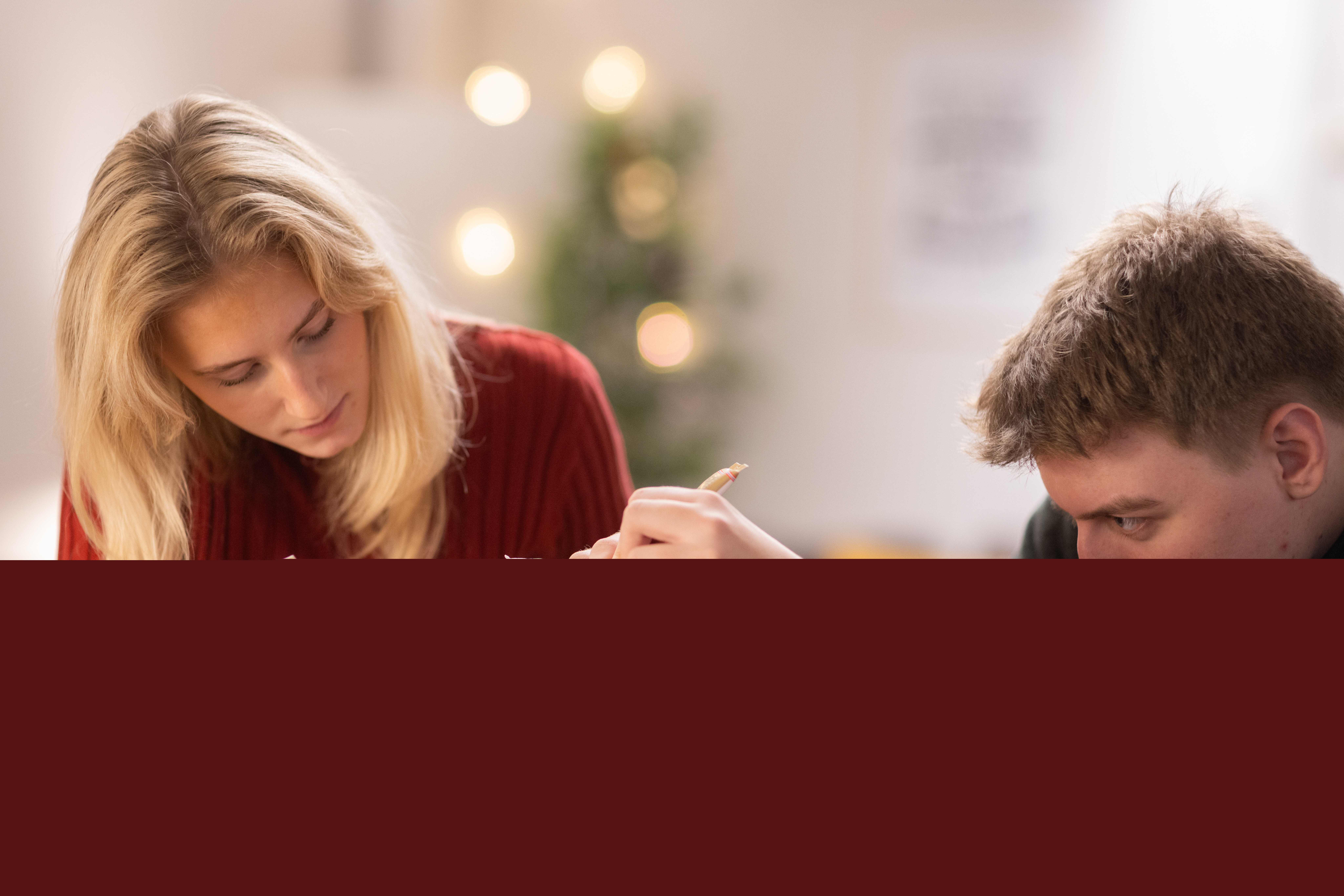 En tjej och en kille i tonåren spritsar ett pepparkakshus.