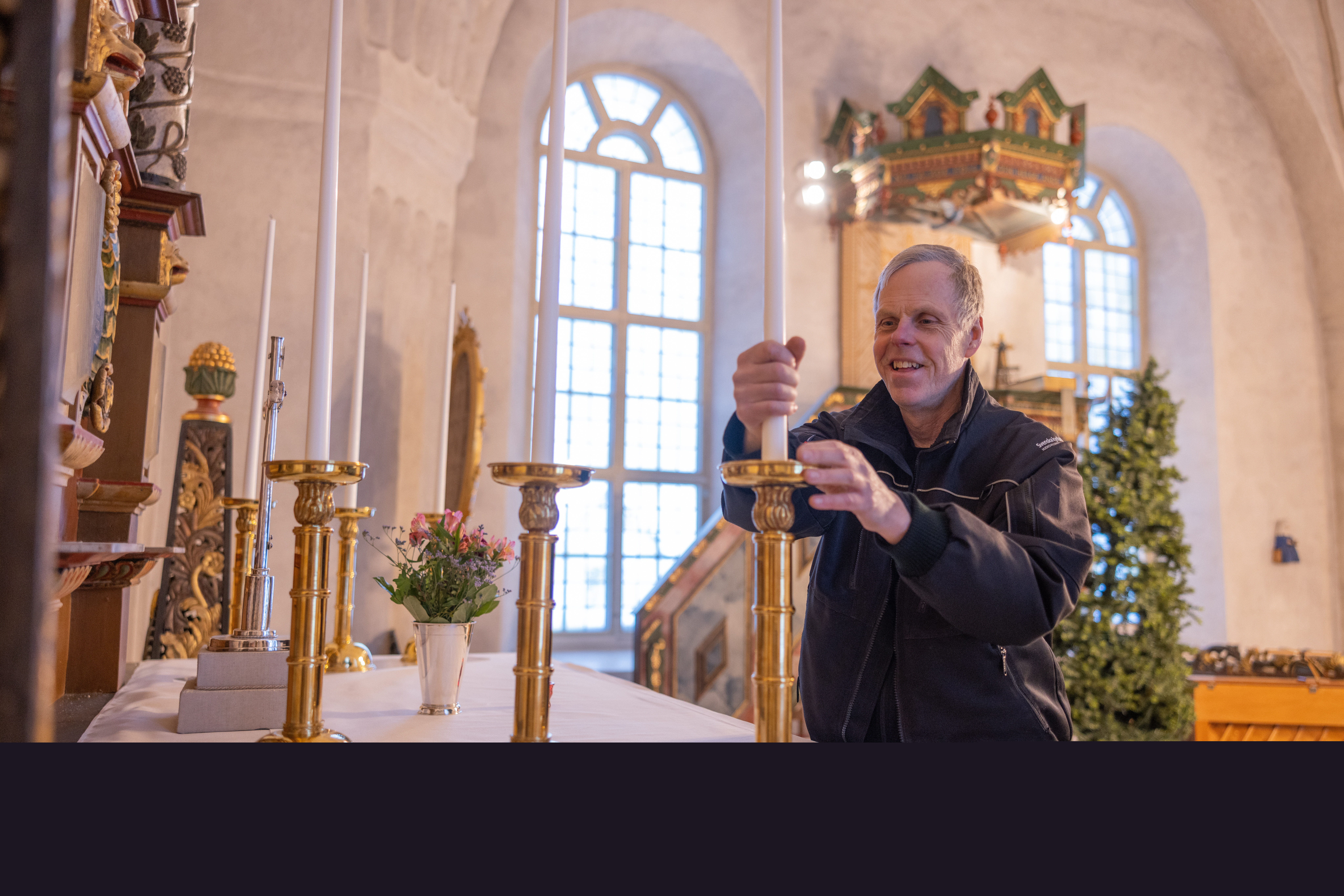En kyrkvaktmästare sätter långa stearin ljus i de gyllene ljusstakarna på kyrkans altare.