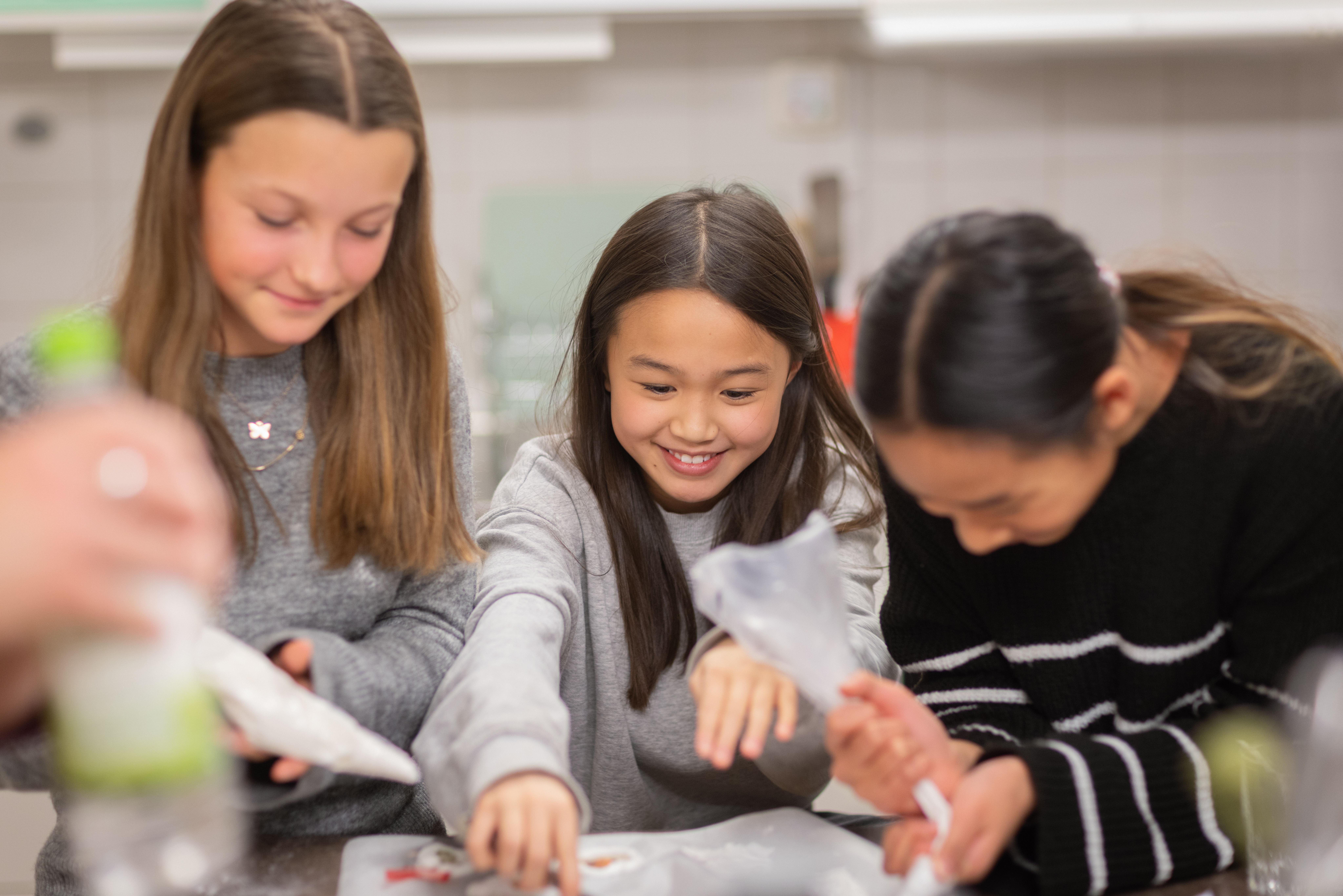 Tre skrattande flickor spritsar i ett kök.