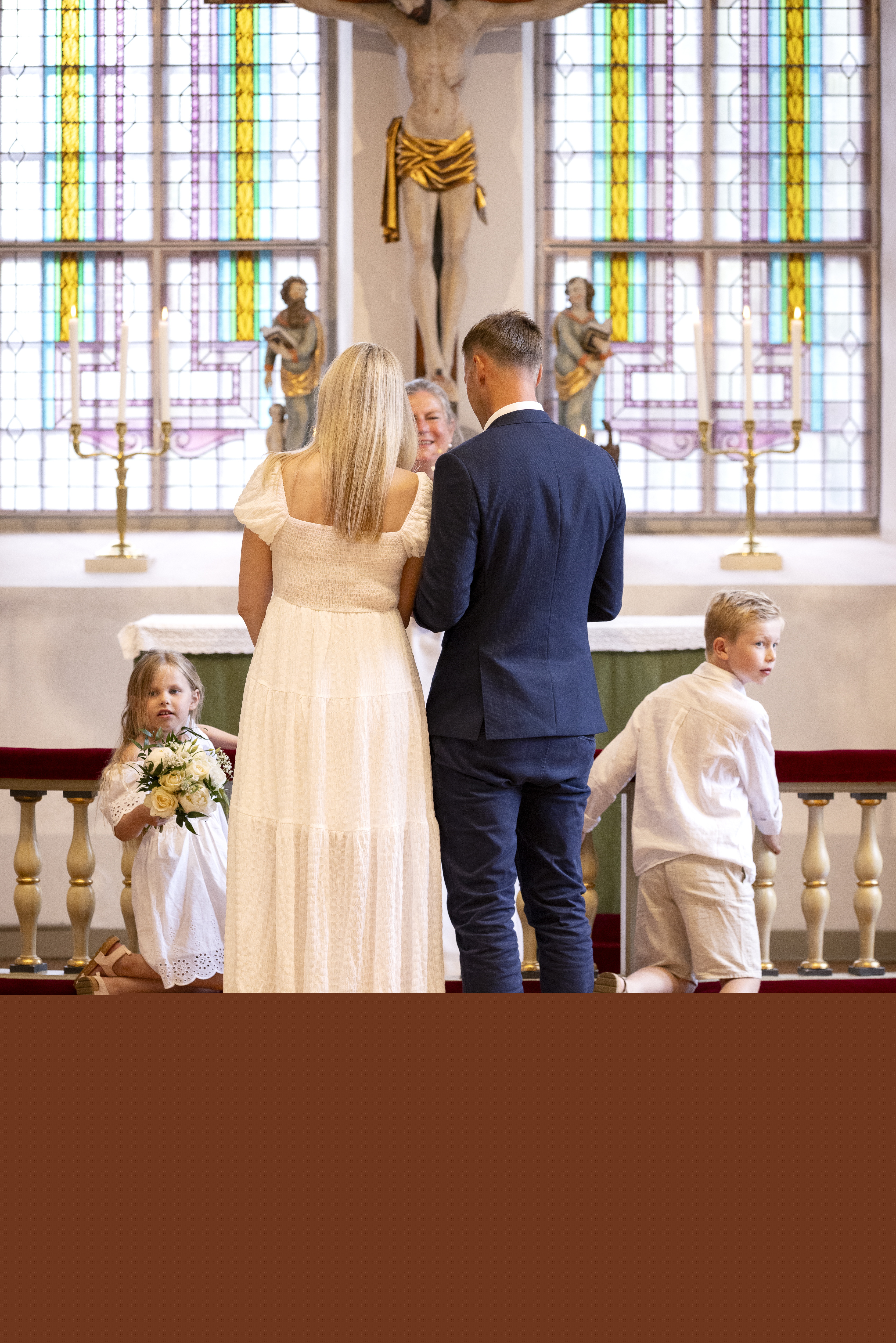 Drop-in vigsel i en kyrka. Brudparet står med ryggen mot kameran. Två barn i bakgrunden.