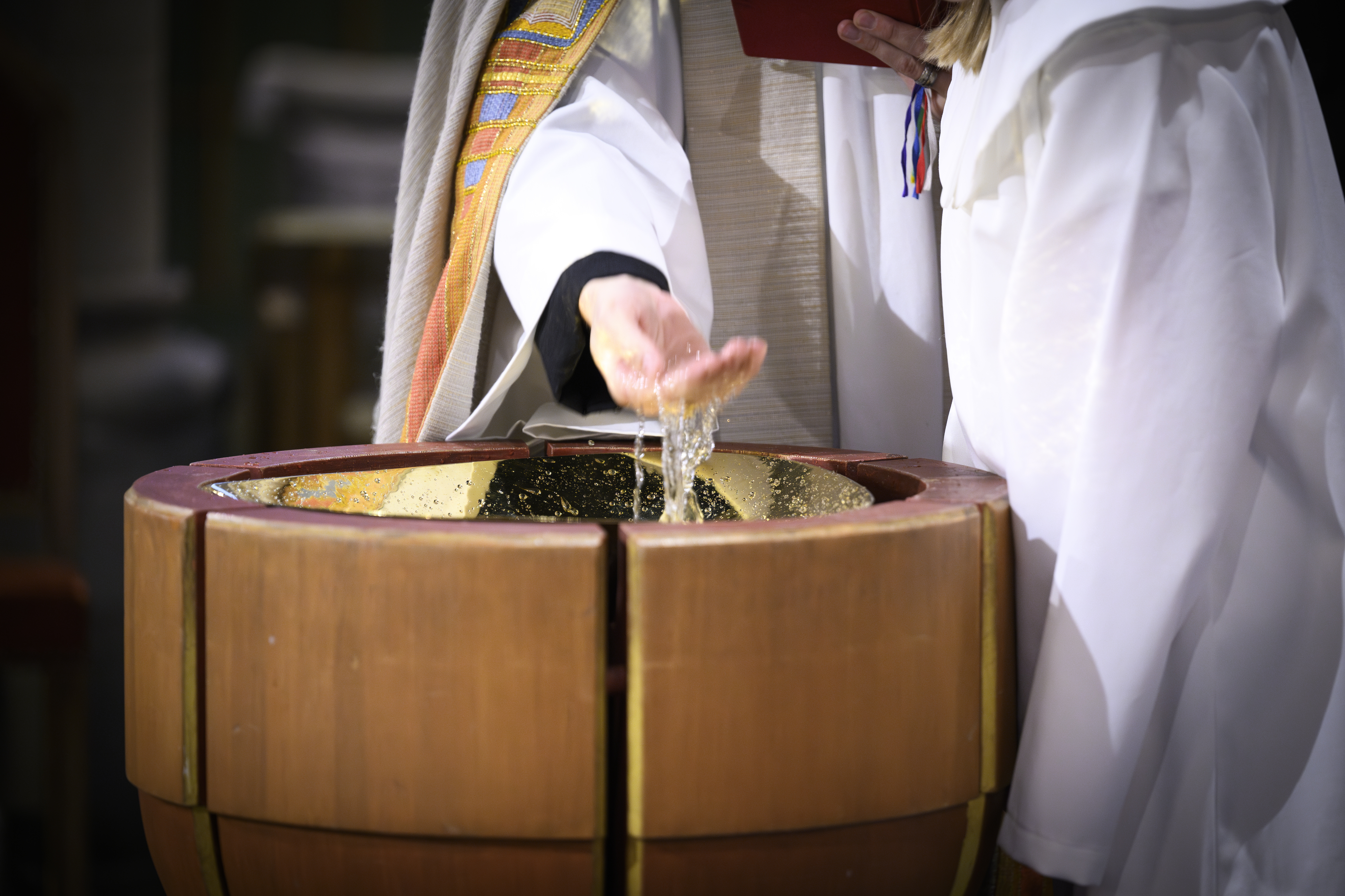 En präst står vid en dopfunt och kupar sin hand i vattnet.