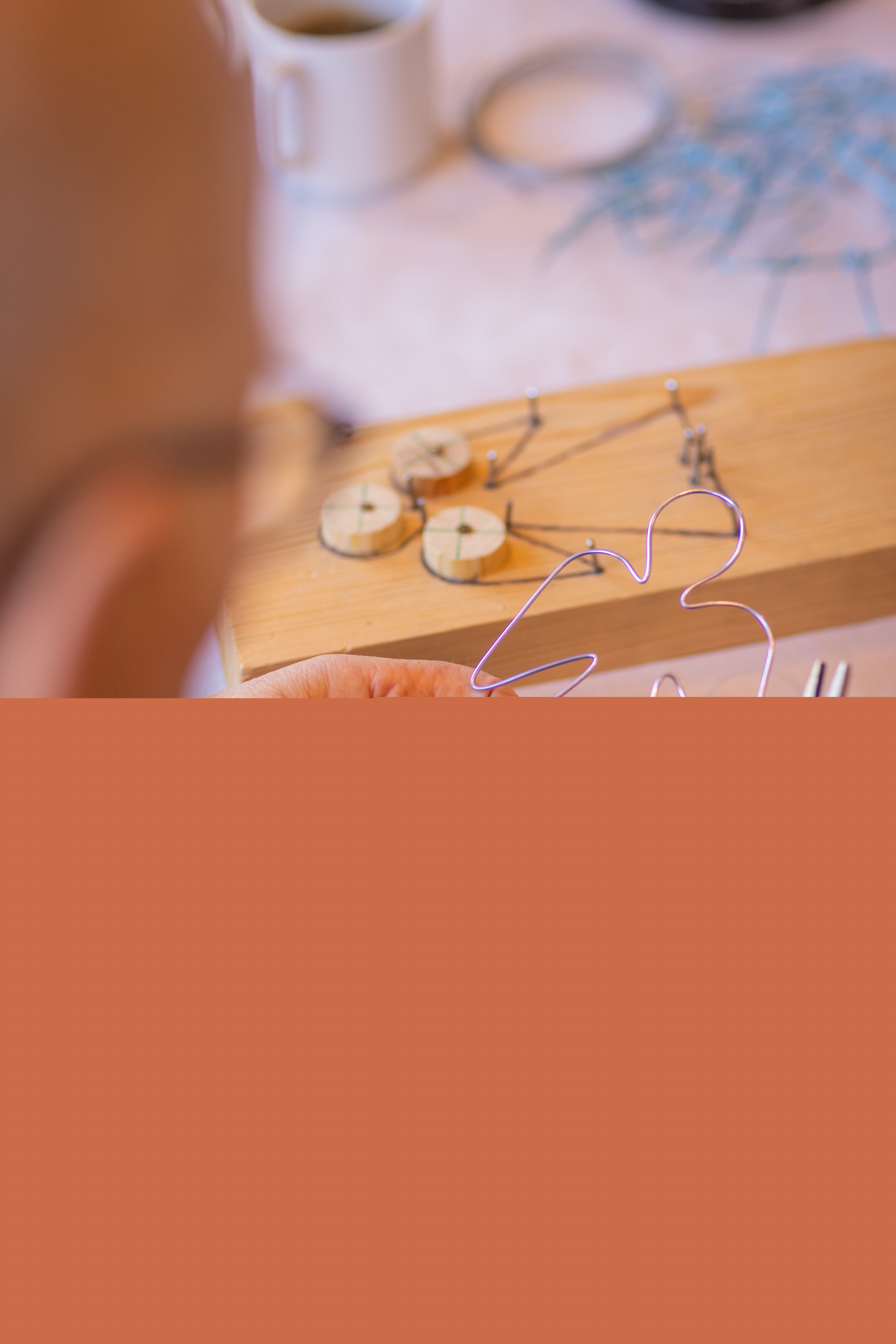 Ett hantverk i trä och ståltråd föreställande en ängel ligger på ett bord. En person i förgrunden håller i en ängel gjord av ståltråd.