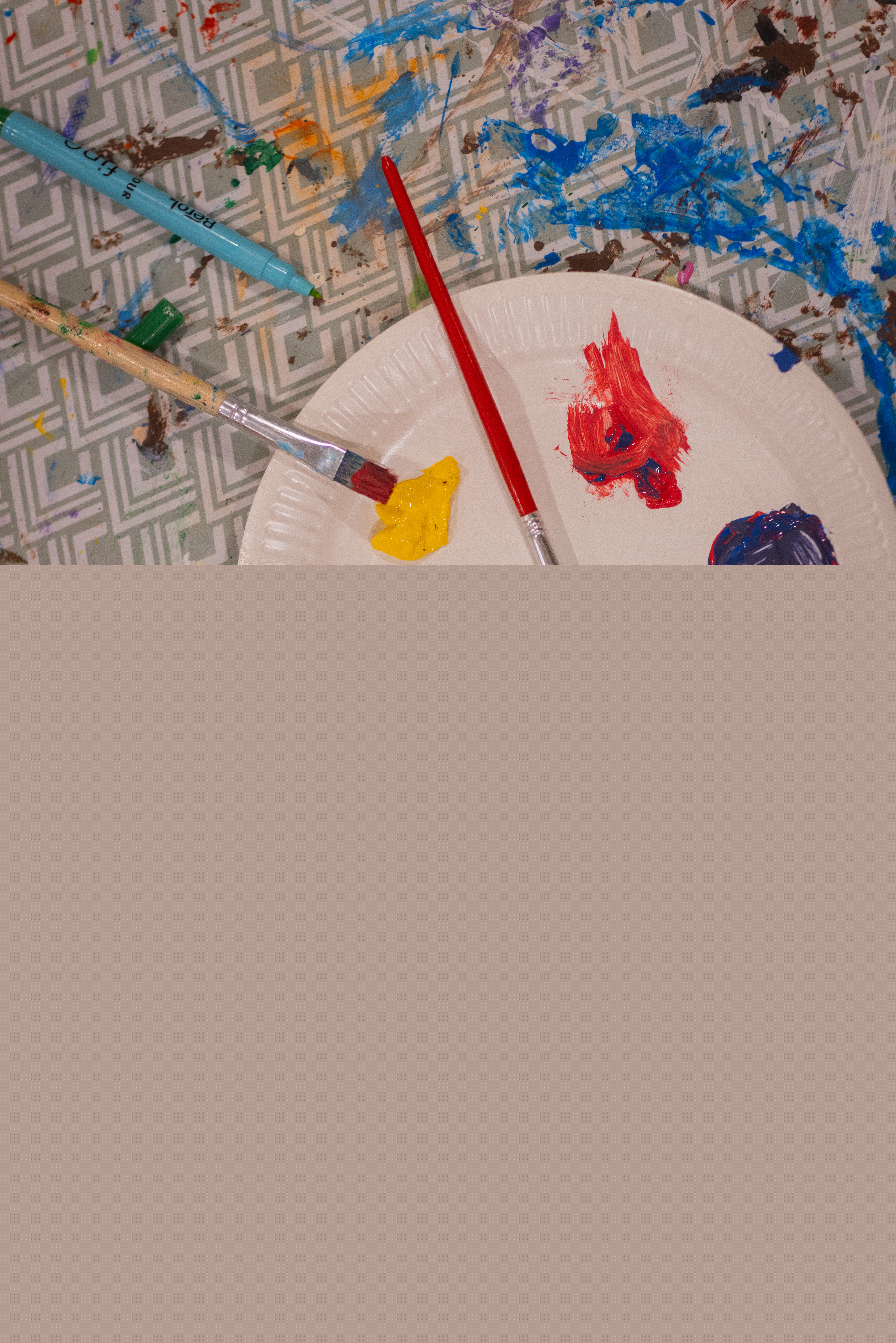 Två papperstallrikar med målarfärg på står på ett bord. Målarpenslar i olika storlekar ligger i närheten.