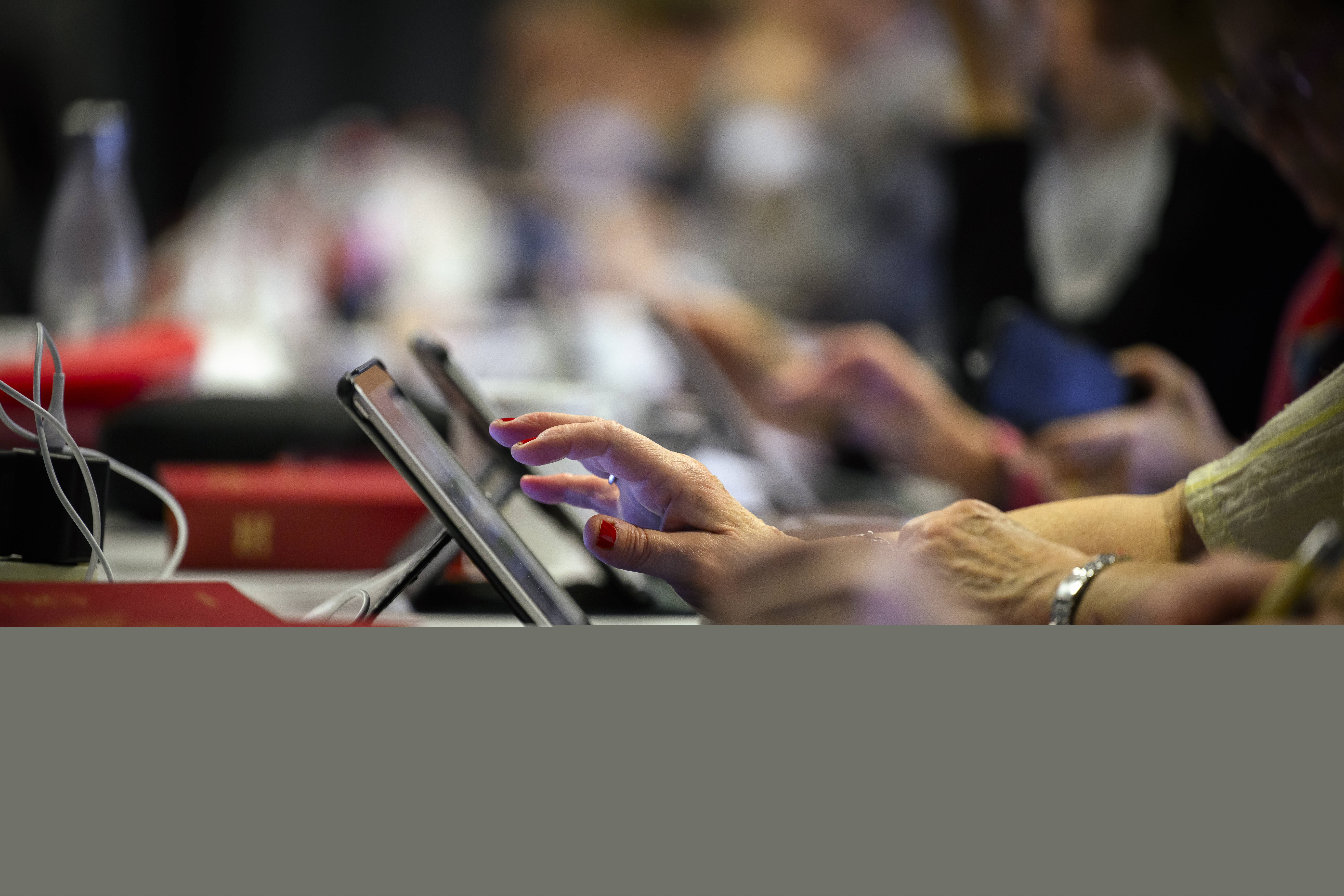 Personer sitter framför sina läsplattor. Psalmböcker ligger på bordet.