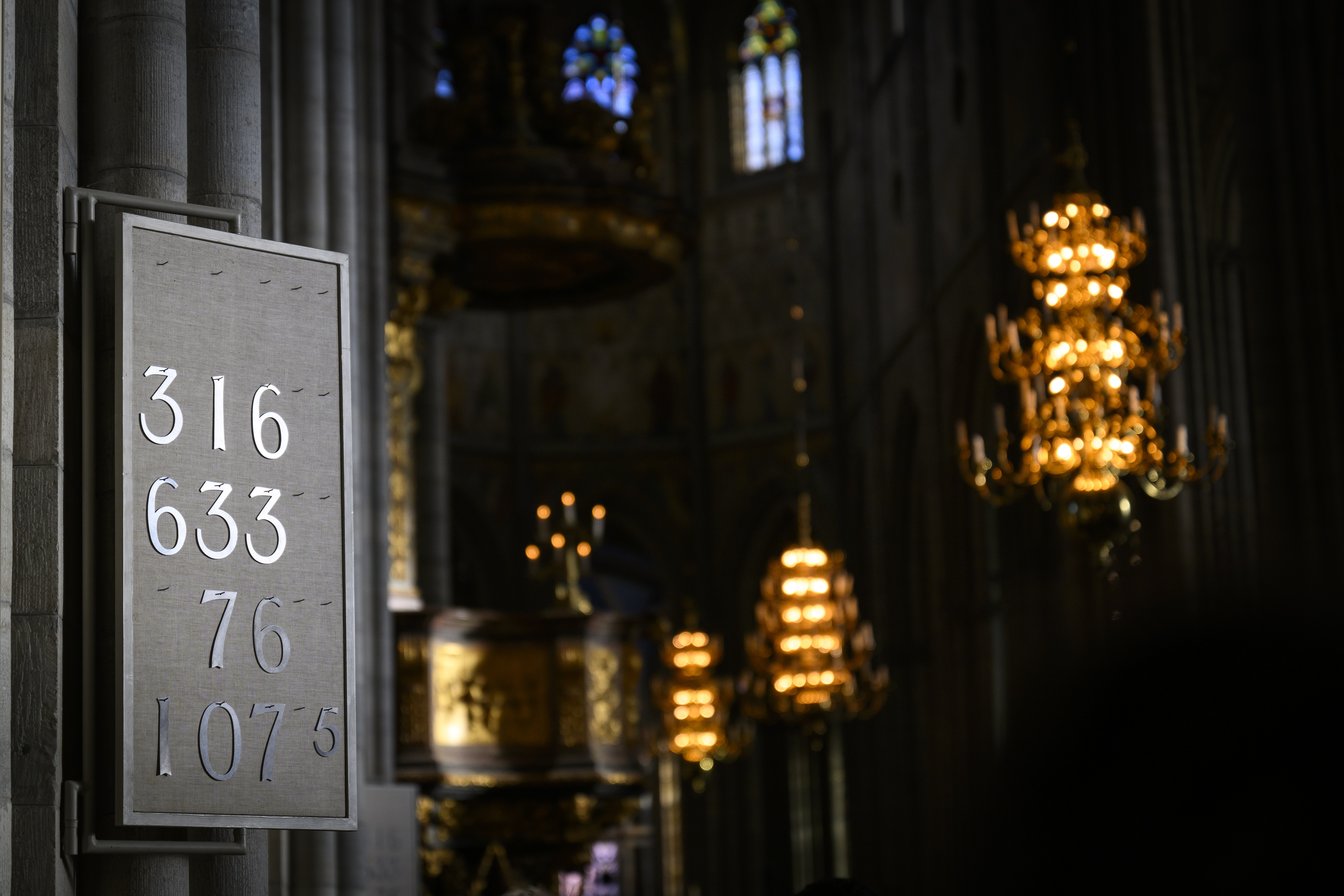 En psalmtavla och ljuskronor som lyser i bakgrunden.
