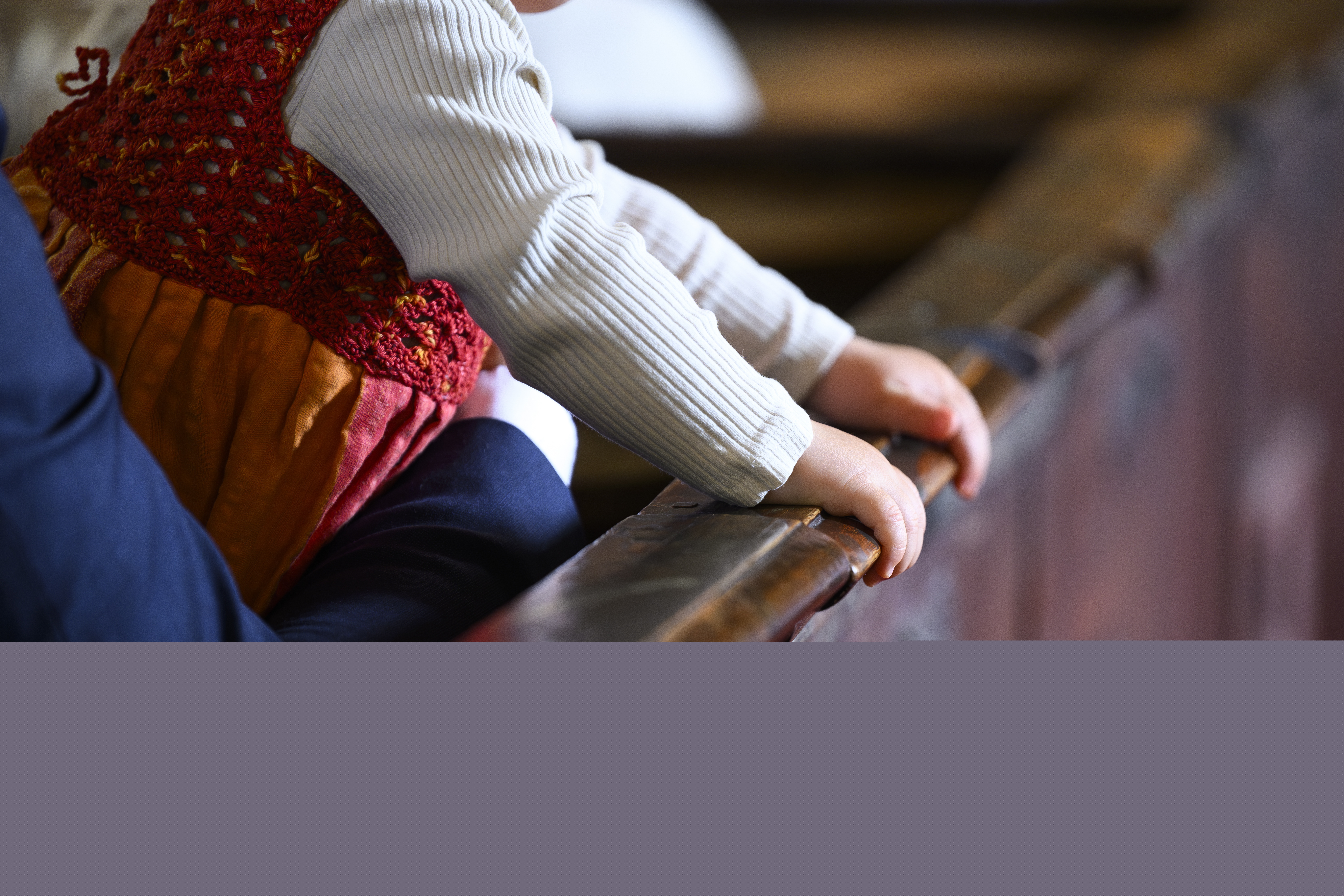 Ett litet barn är i famnen på en person som sitter i kyrkbänken. Barnet håller sina händer på kyrkbänksdörren.