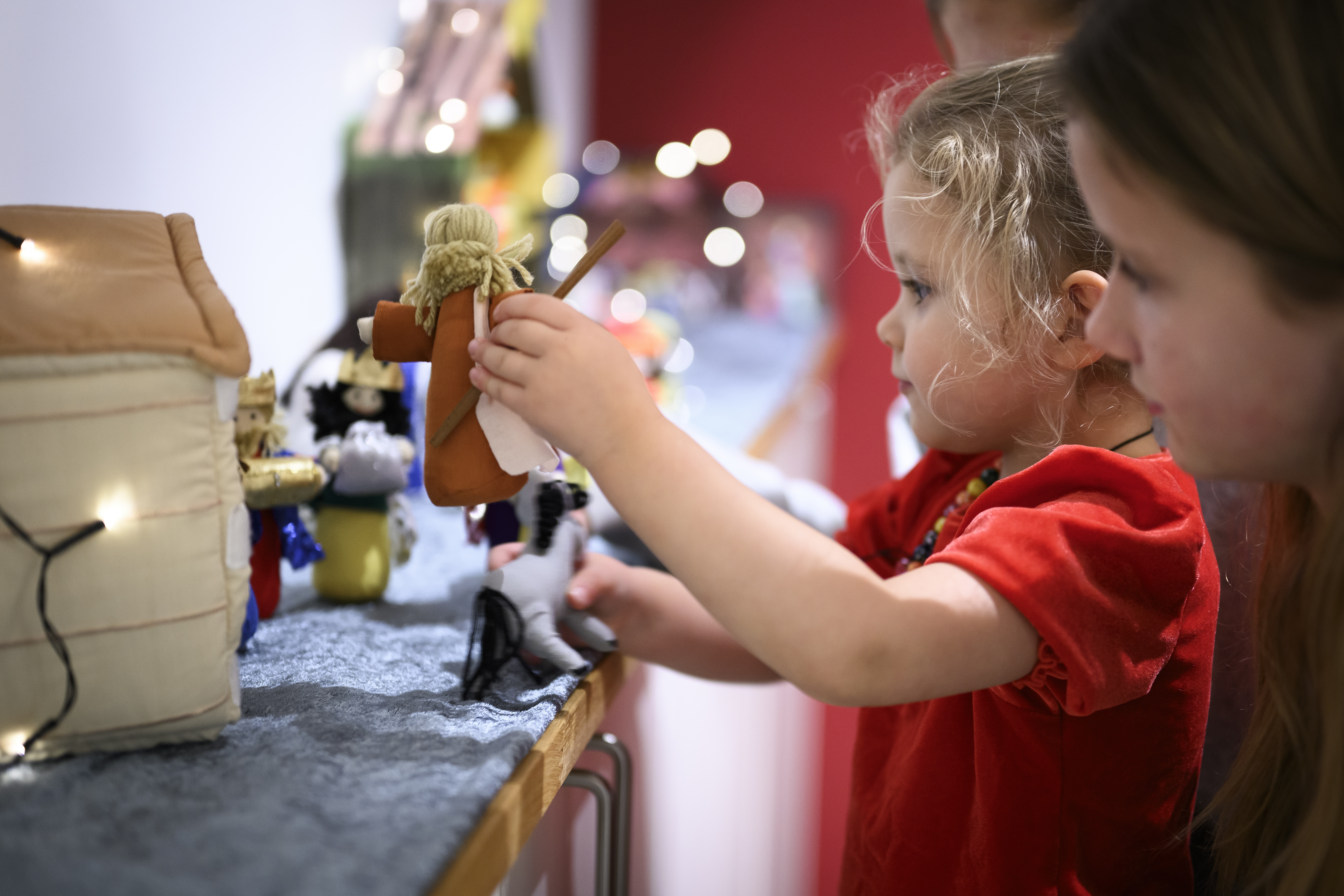 Ett litet barn i röd tröja leker med en julkrubba i mjukistyg.