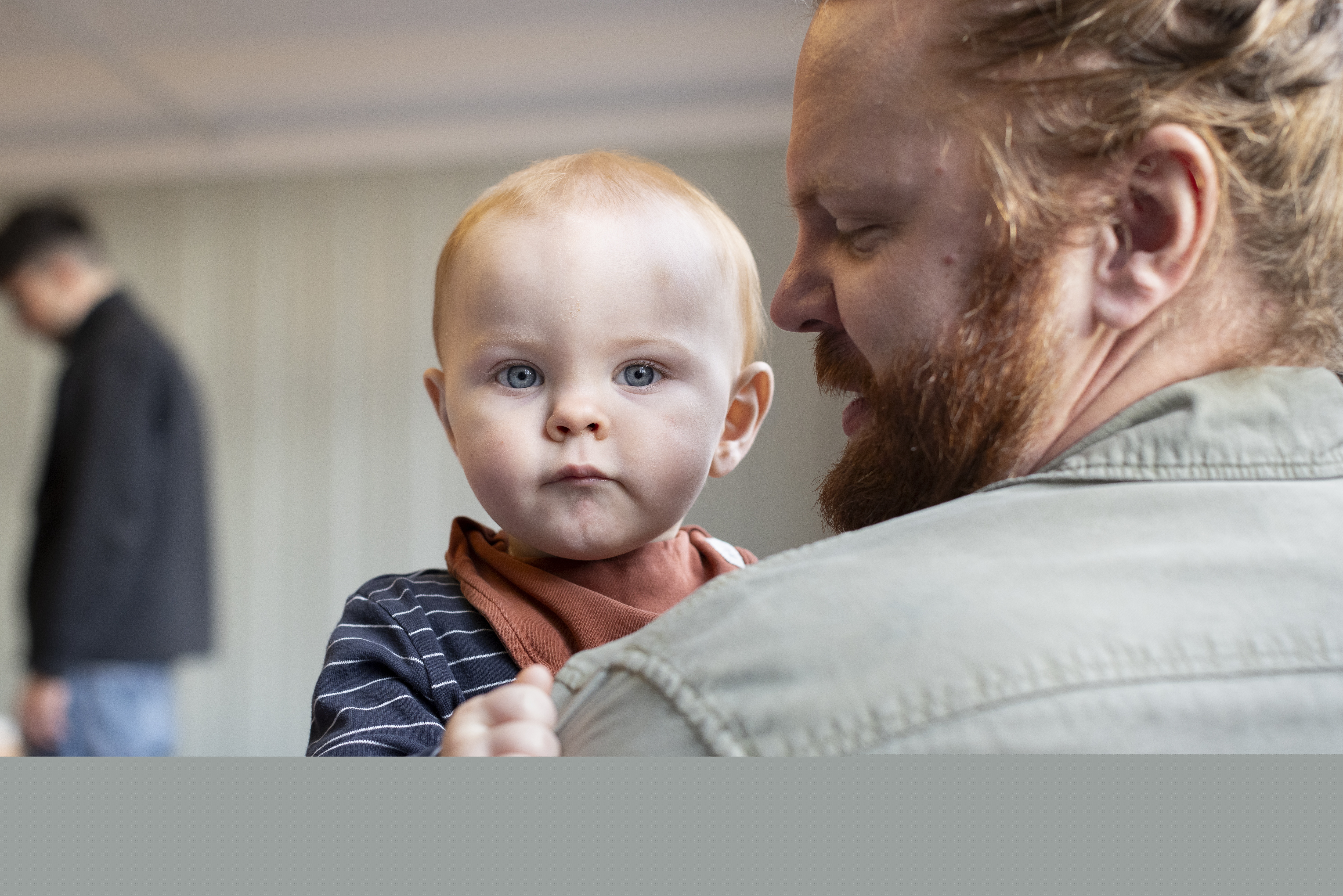 Närbild på ett barn som tittar in i kameran över en mans axel.