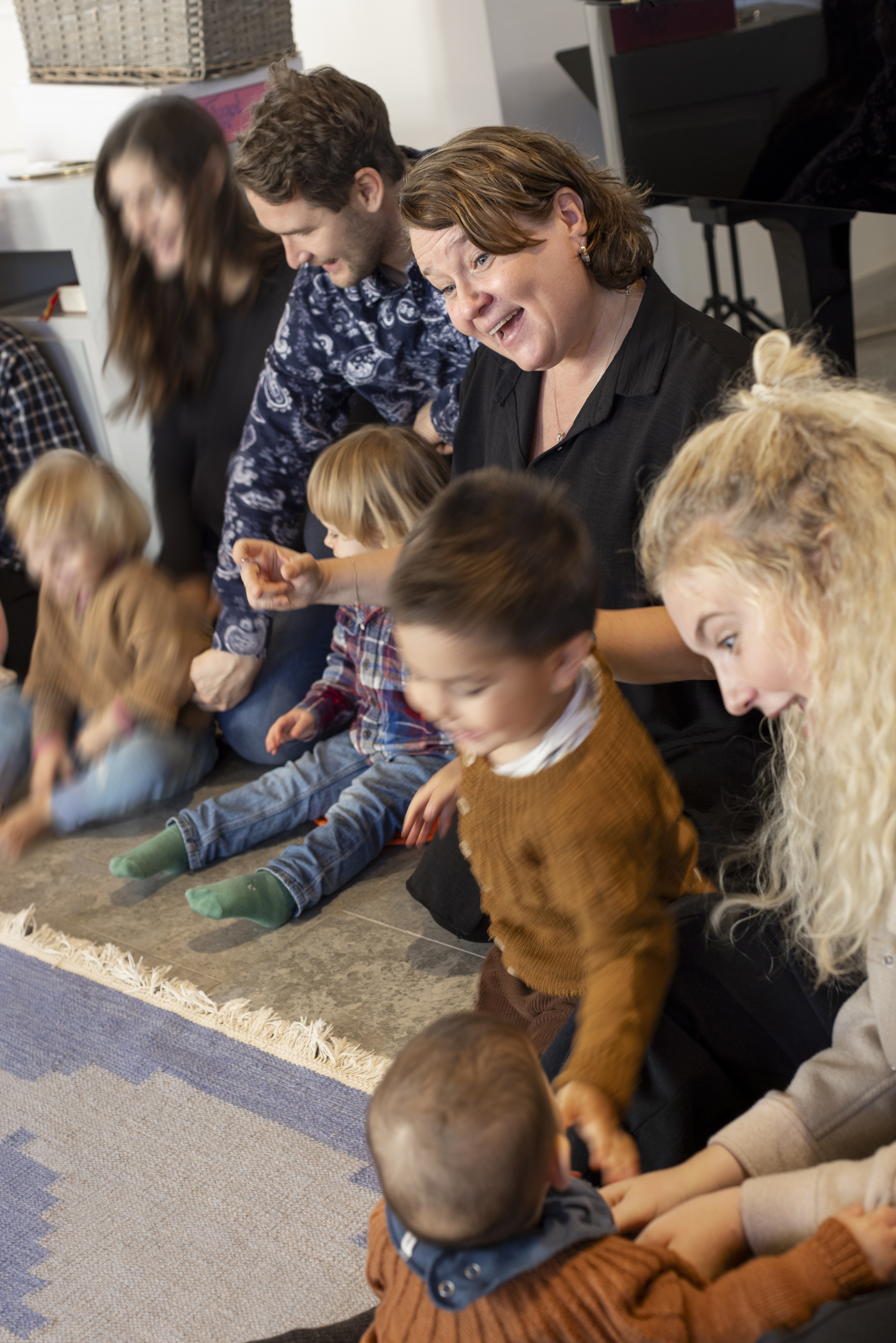 En man, tre kvinnor och flera barn sitter på golvet och sjunger tillsammans.
