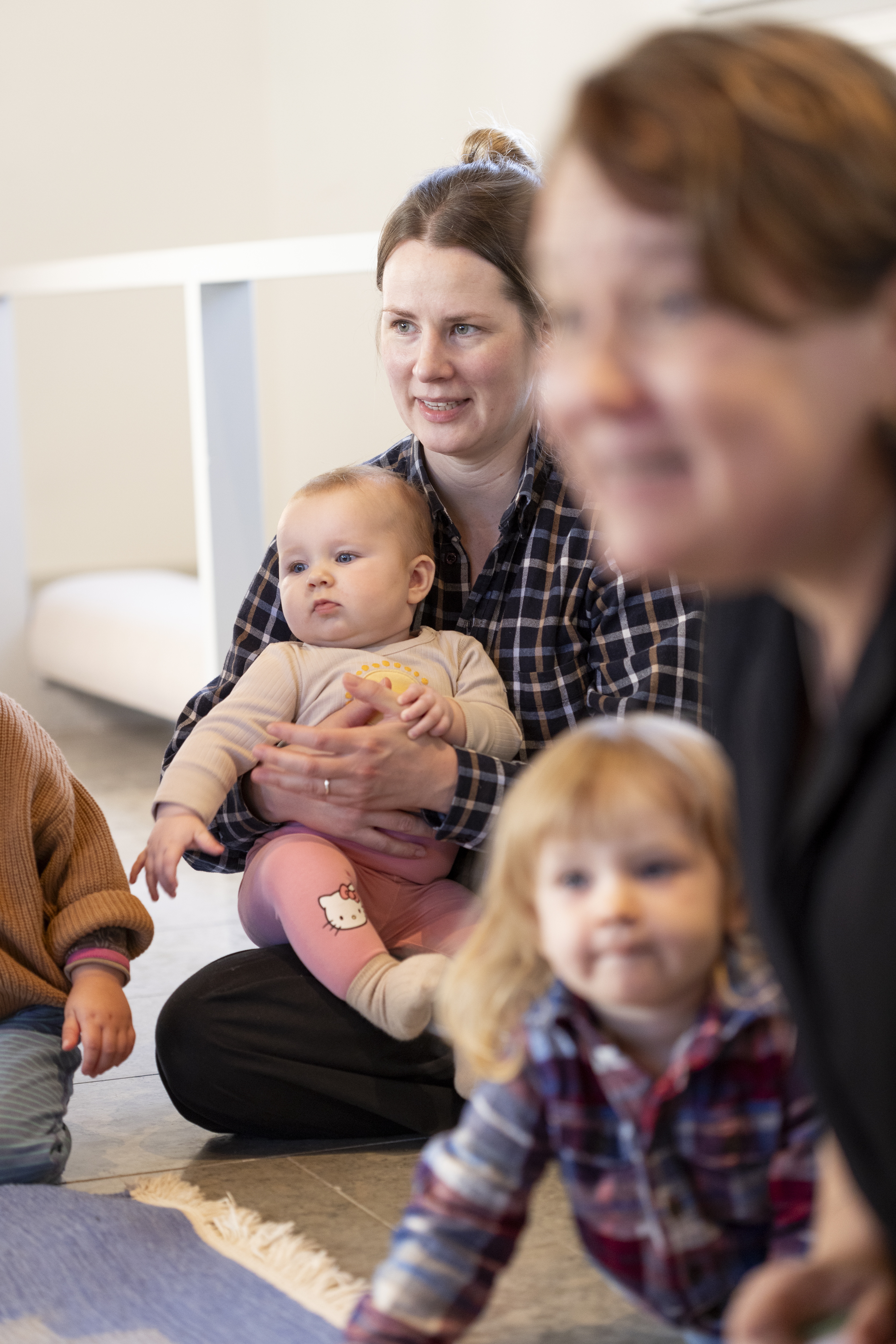 En kvinna sitter på golvet med ett litet barn i knät. En annan kvinna och ett barn i förgrunden.