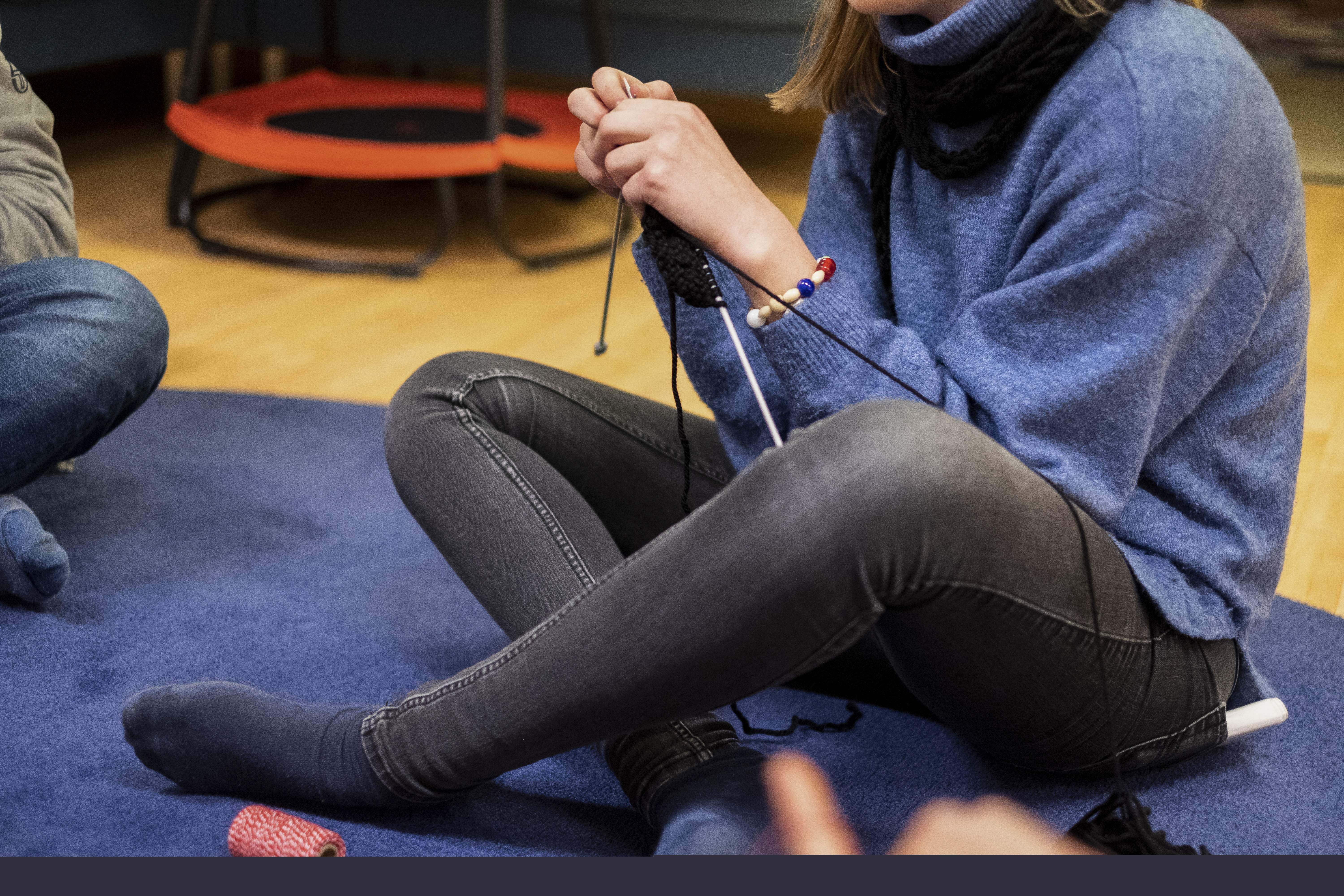 En person sitter på golvet och stickar, med frälsarkransen runt vänster handled.