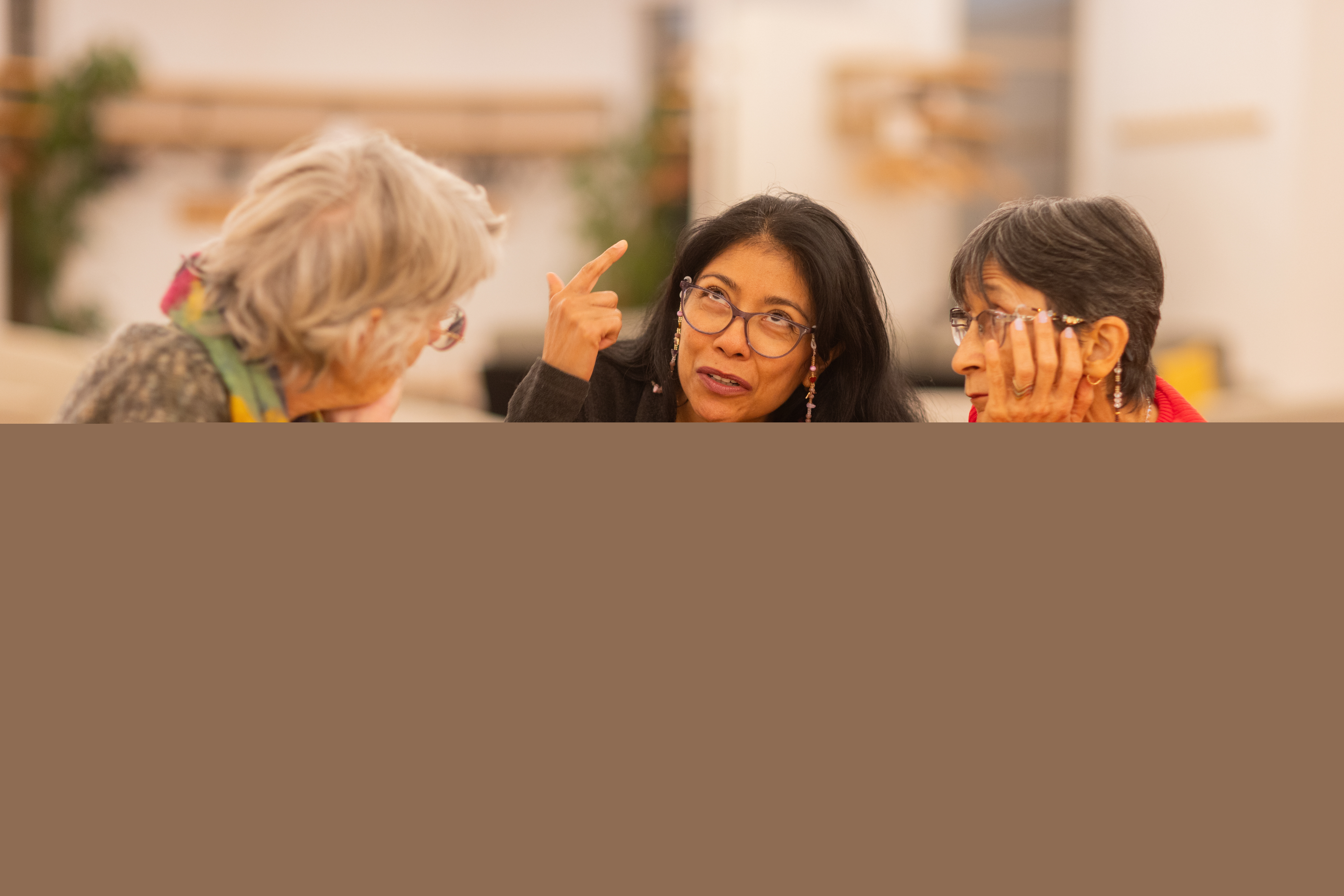 Tre kvinnor sitter vid ett runt bord och samtalar med varandra.