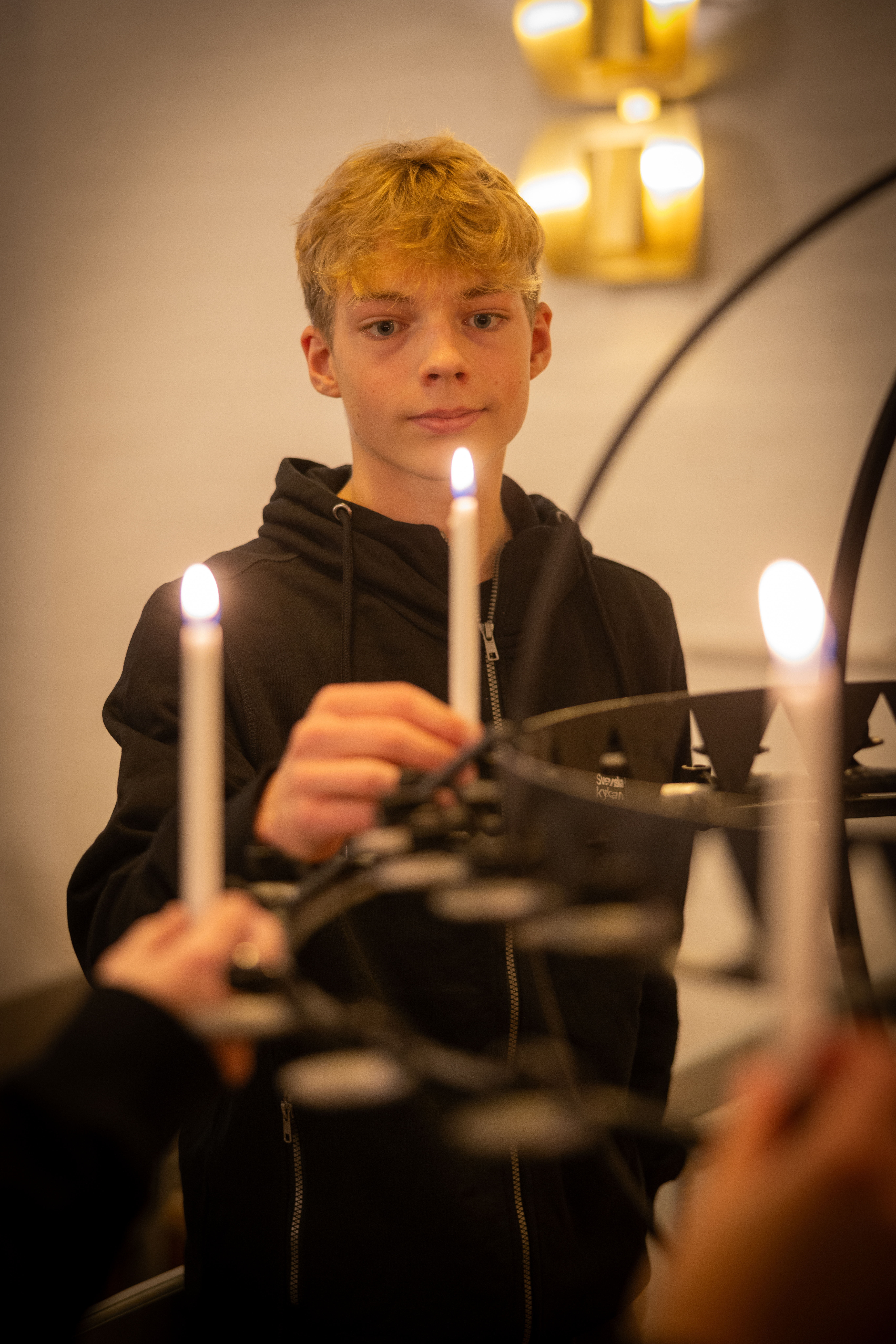 En ung kille står framför en ljusbärare och sätter ner ett tänt ljus.