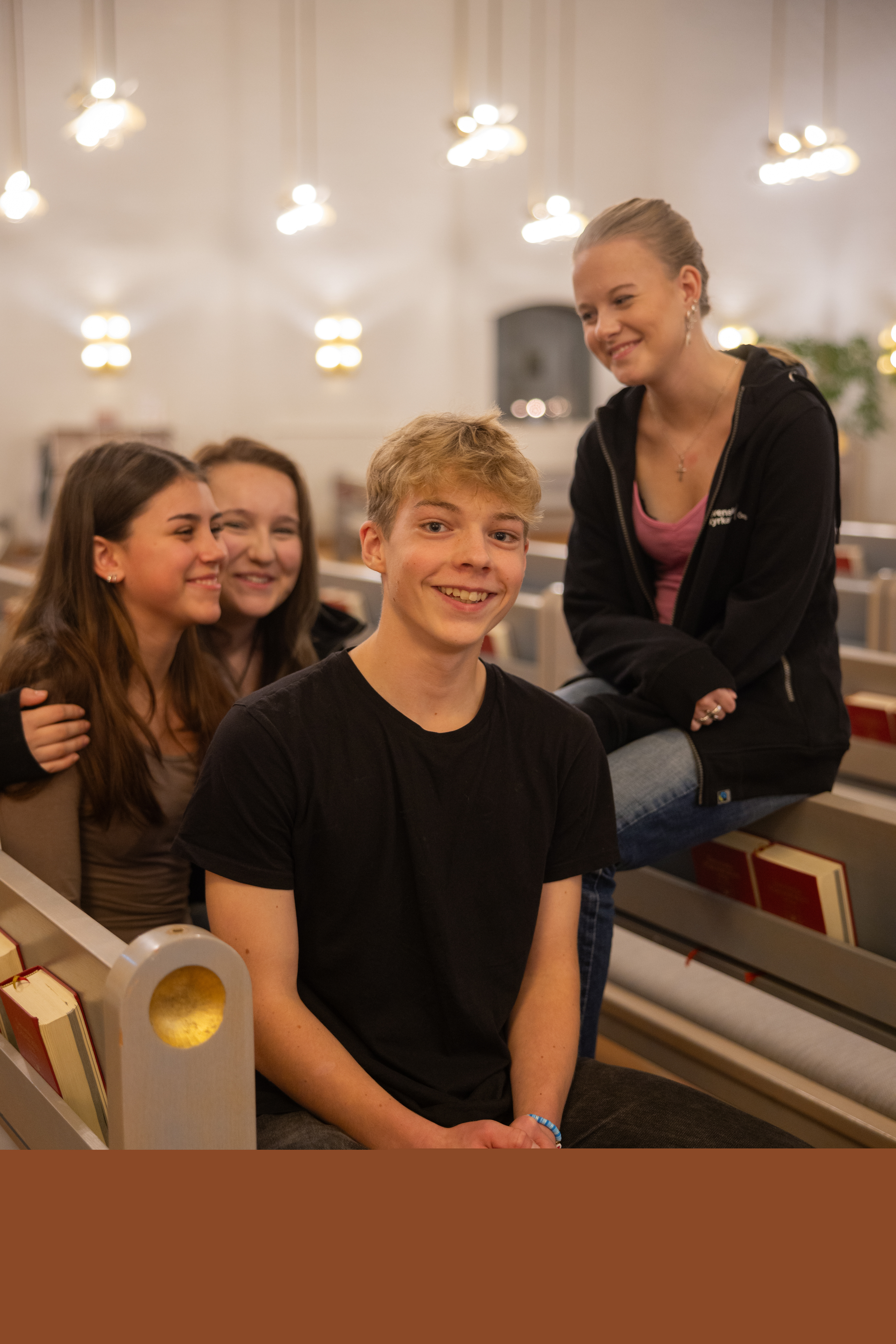Fyra glada ungdomar sitter i kyrkbänken och tittar in i kameran.