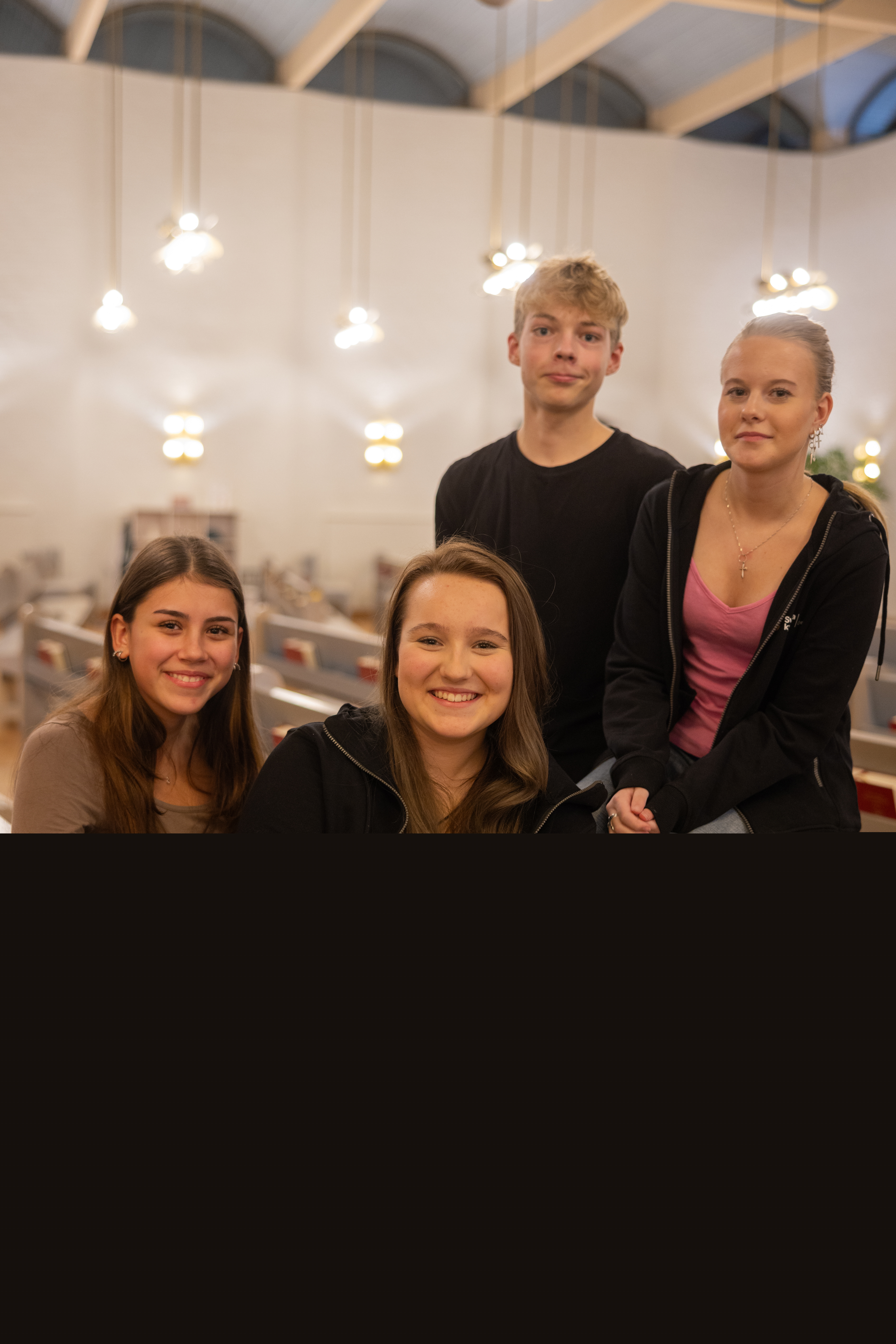 Fyra glada ungdomar sitter i kyrkbänken och tittar in i kameran.