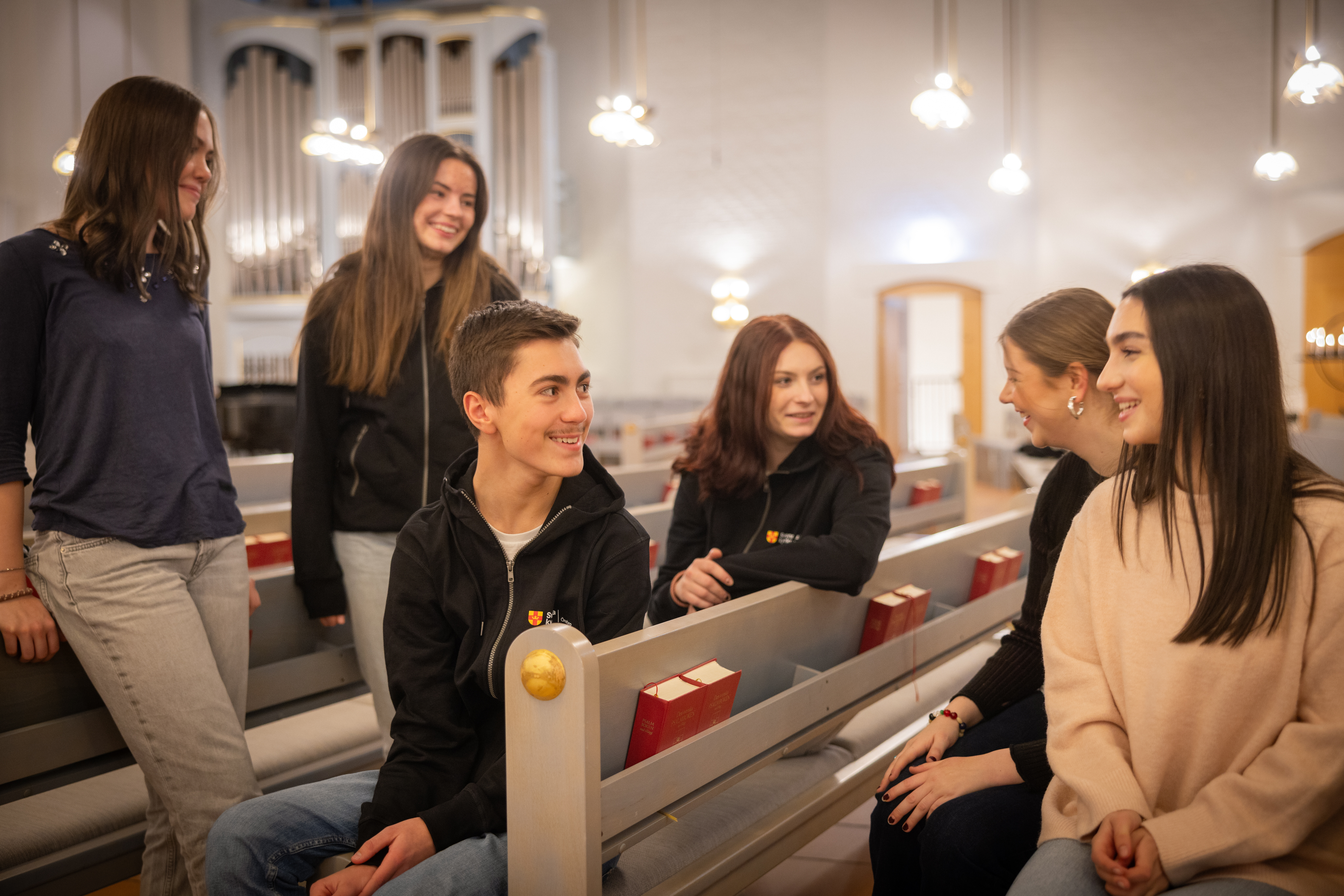 Flera ungdomar samtalar med varandra i en kyrka. Biblar utställda i bänkraderna.