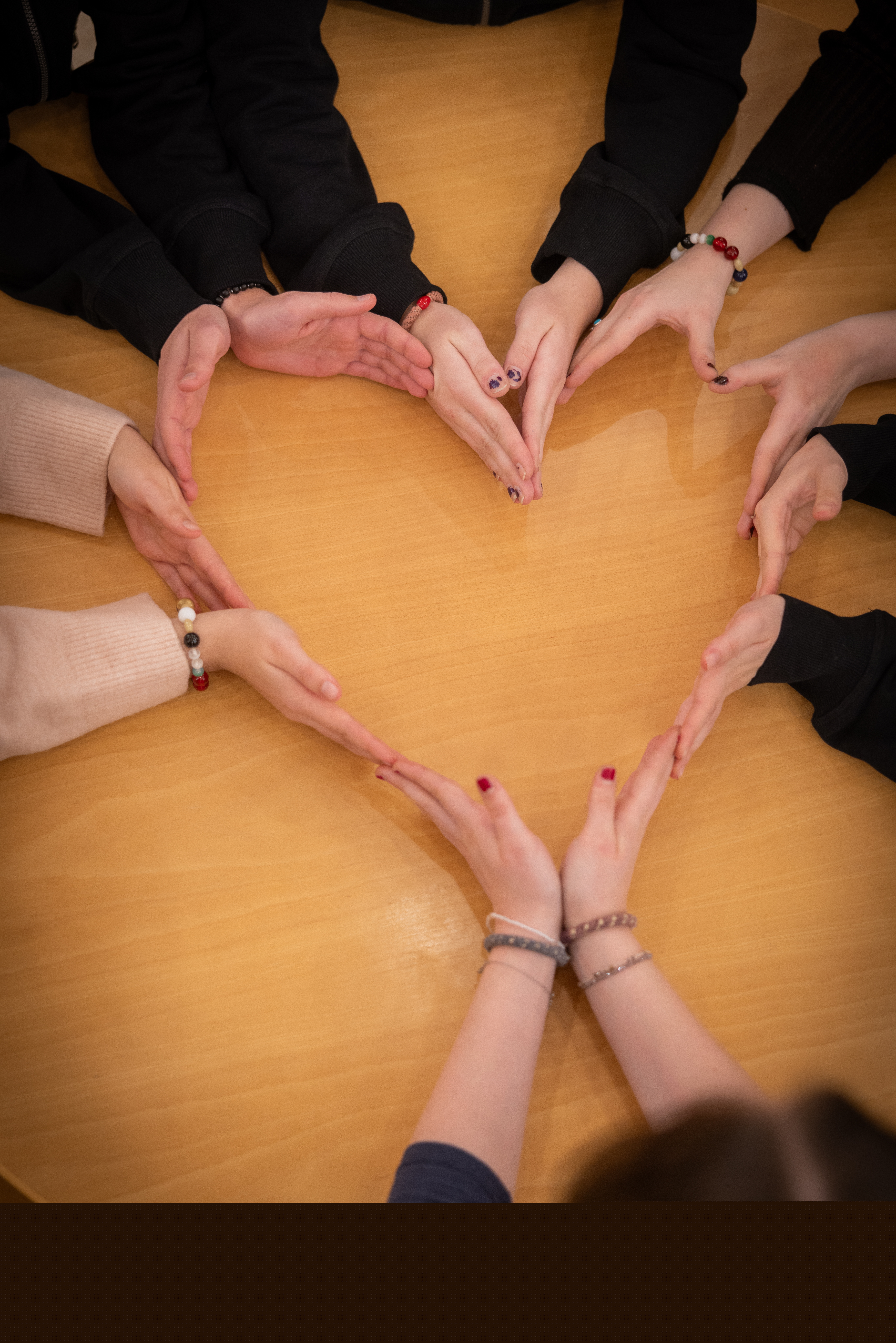 Flera personer sitter vid ett bord och formar  ett hjärta med hjälp av sina händer.