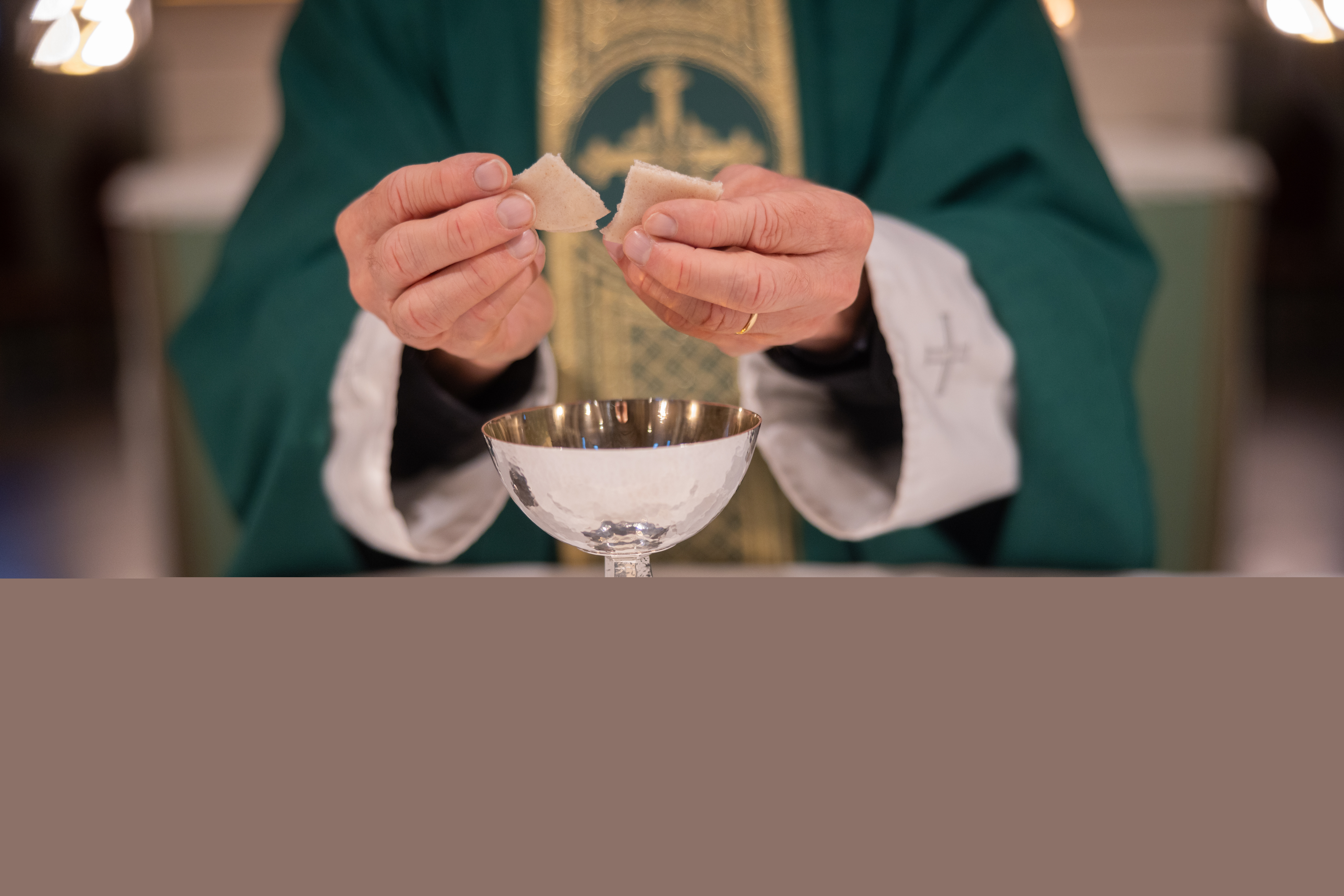 En präst bryter en oblat över nattvardskalken.
