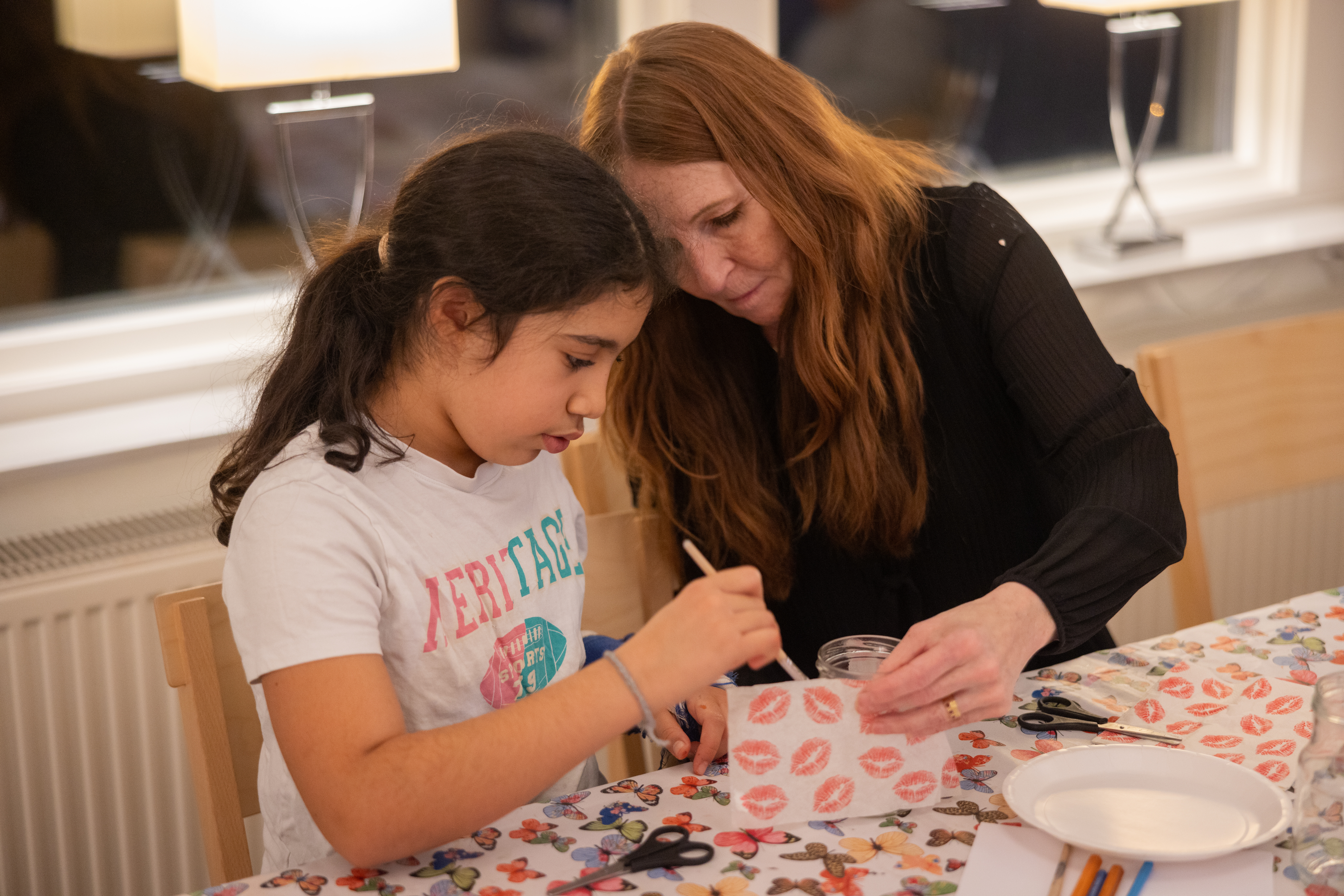 En kvinna sitter och pysslar tillsammans med en ung tjej.