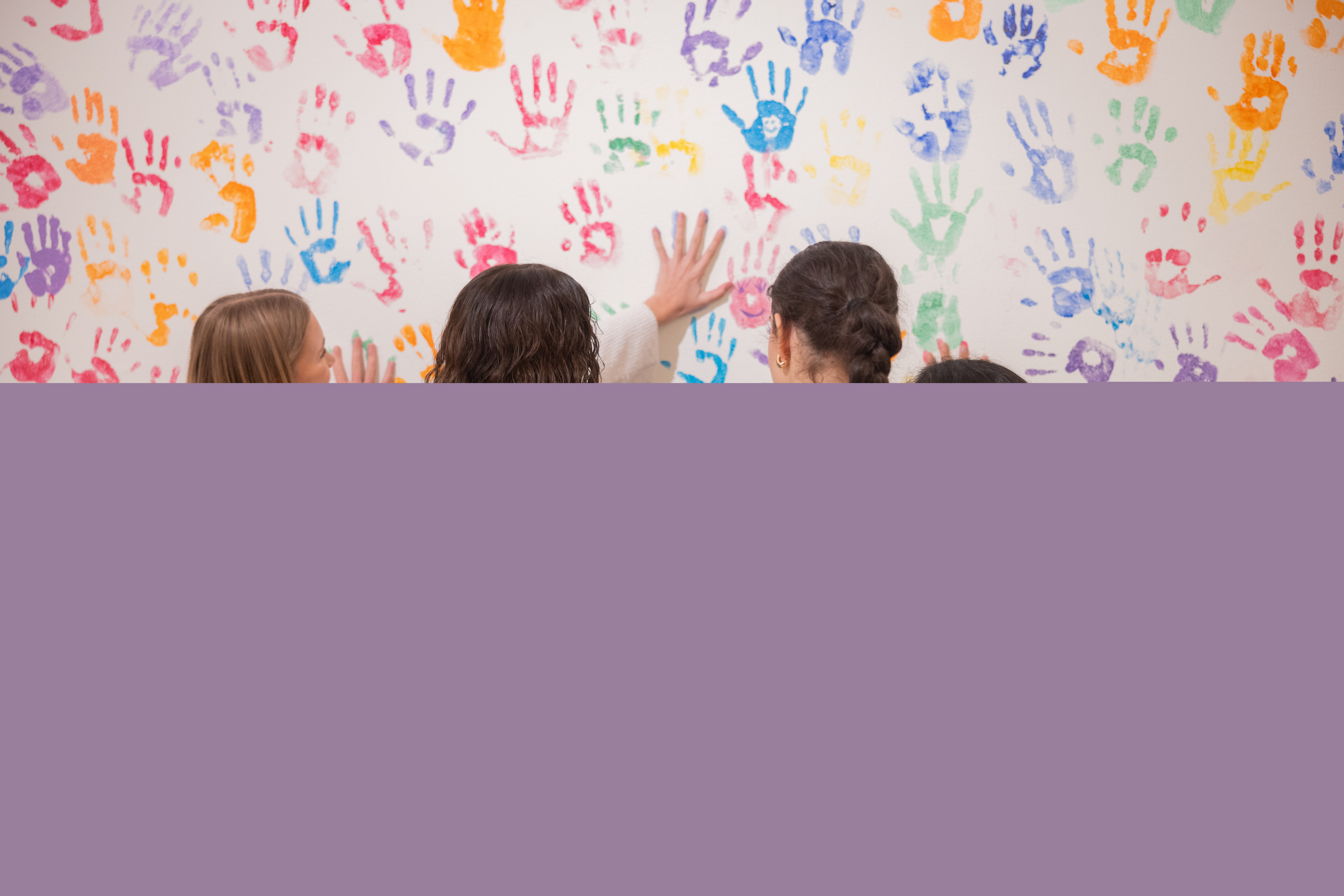 Fyra tjejer har färgat sina händer letar nu tomma ytor på en vägg full av färgglada handavtryck.