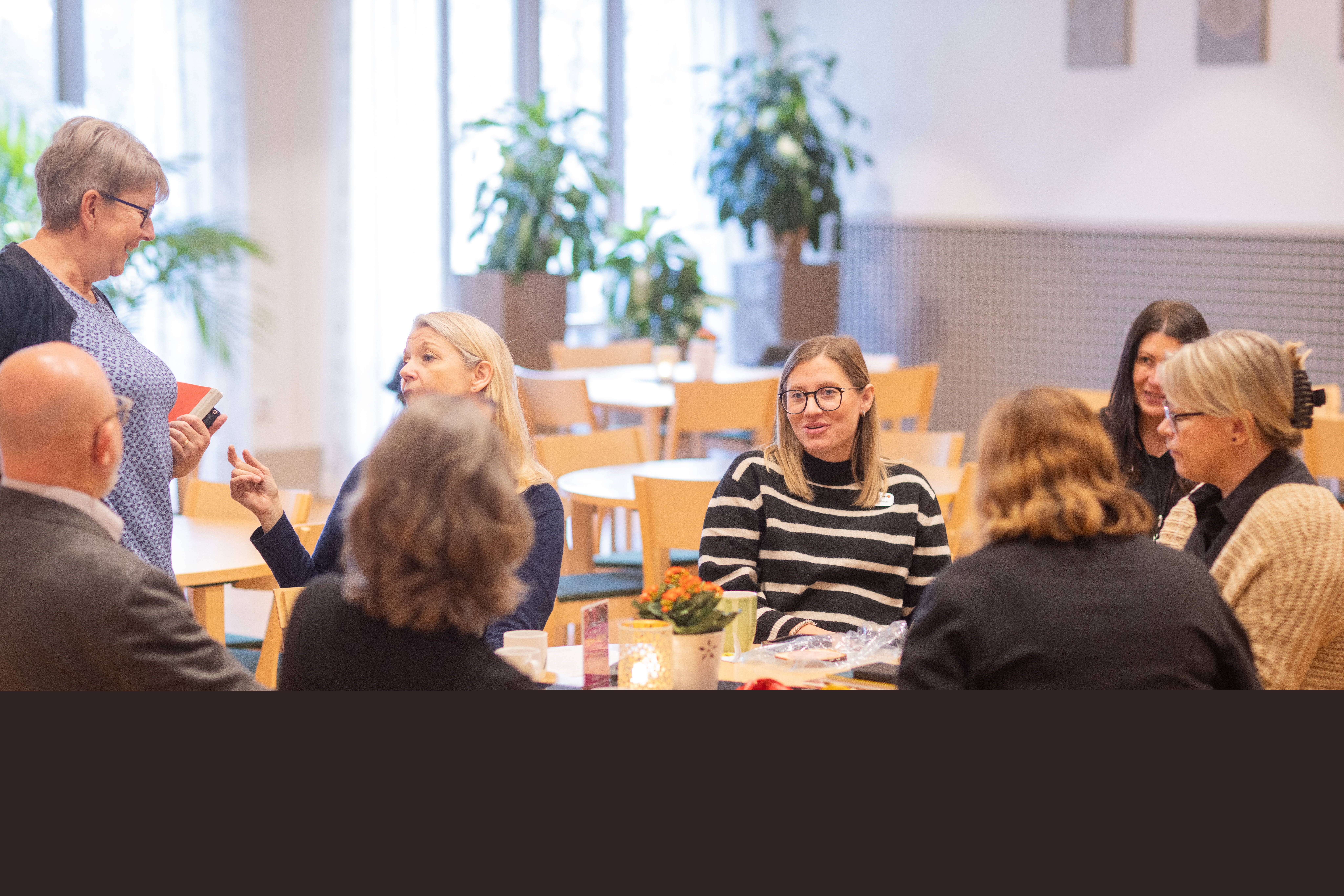 Flera vuxna personer sitter tillsammans vid ett runt bord och samtalar.
