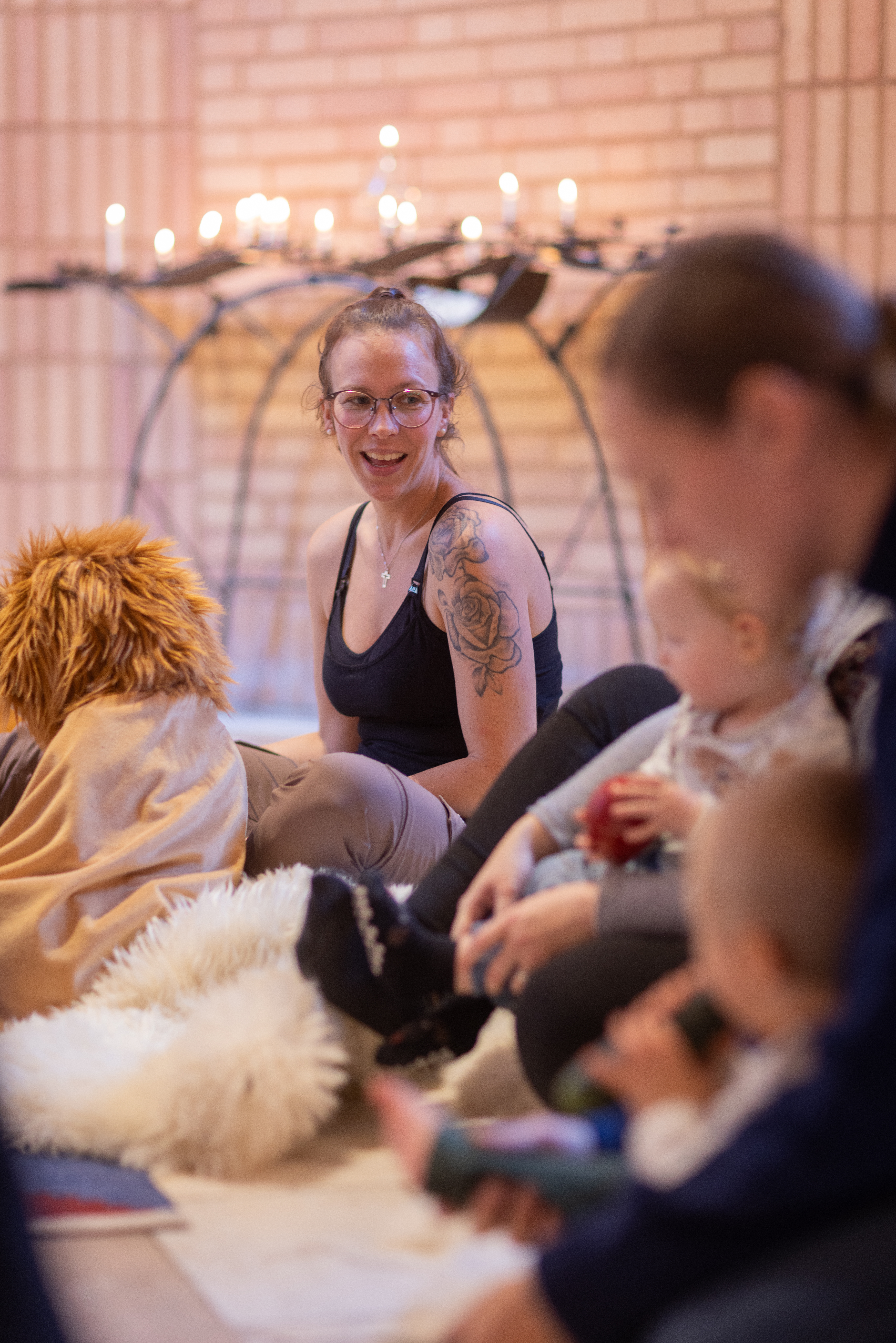 Två kvinnor sitter på golvet och leker med barnen på en öppen förskola. Tända ljus i bakgrunden.